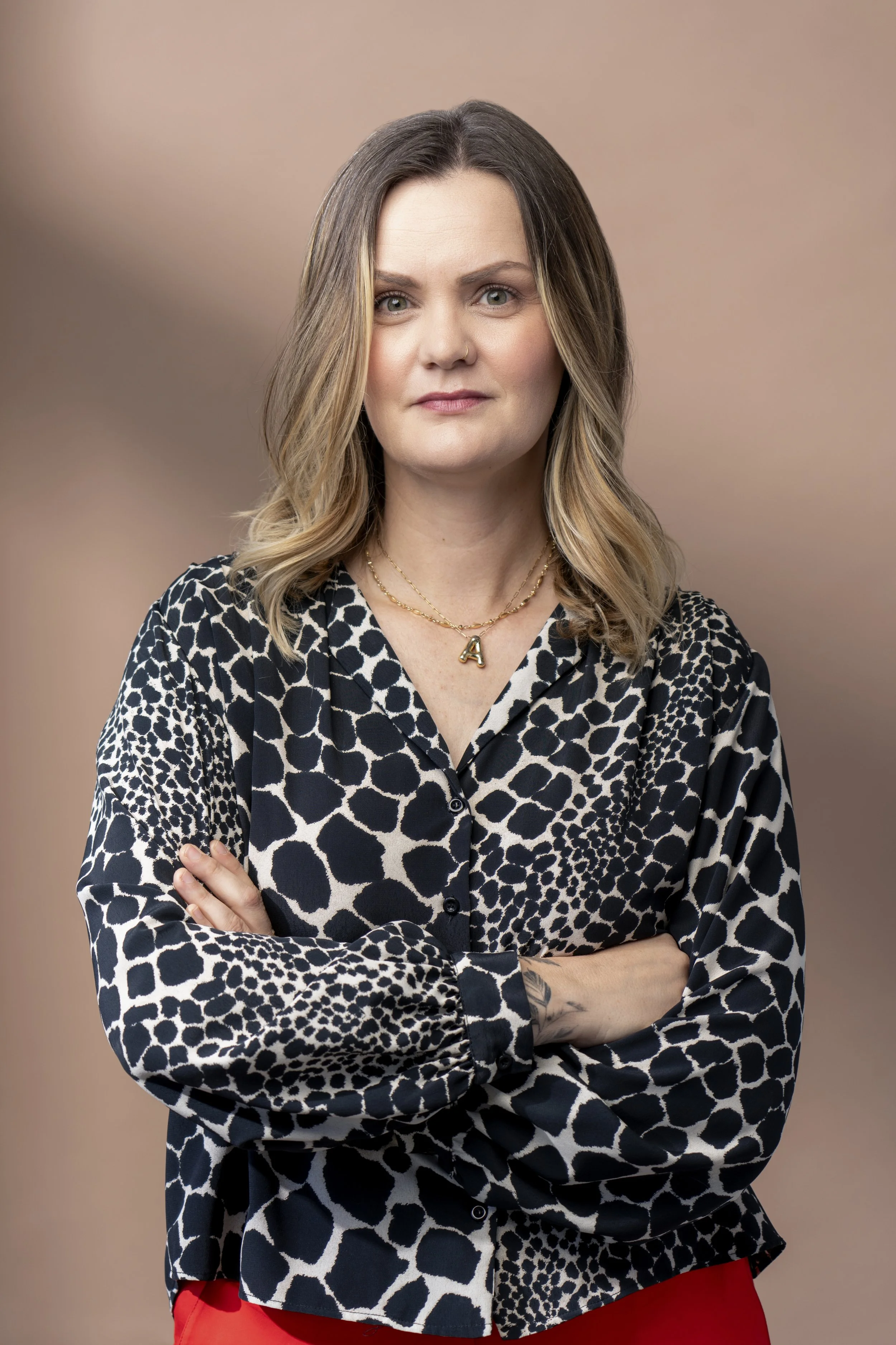 Amanda is wearing a black and white animal print blouse with her arms crossed gently across her chest. She is smiling and looking directly at the camera.