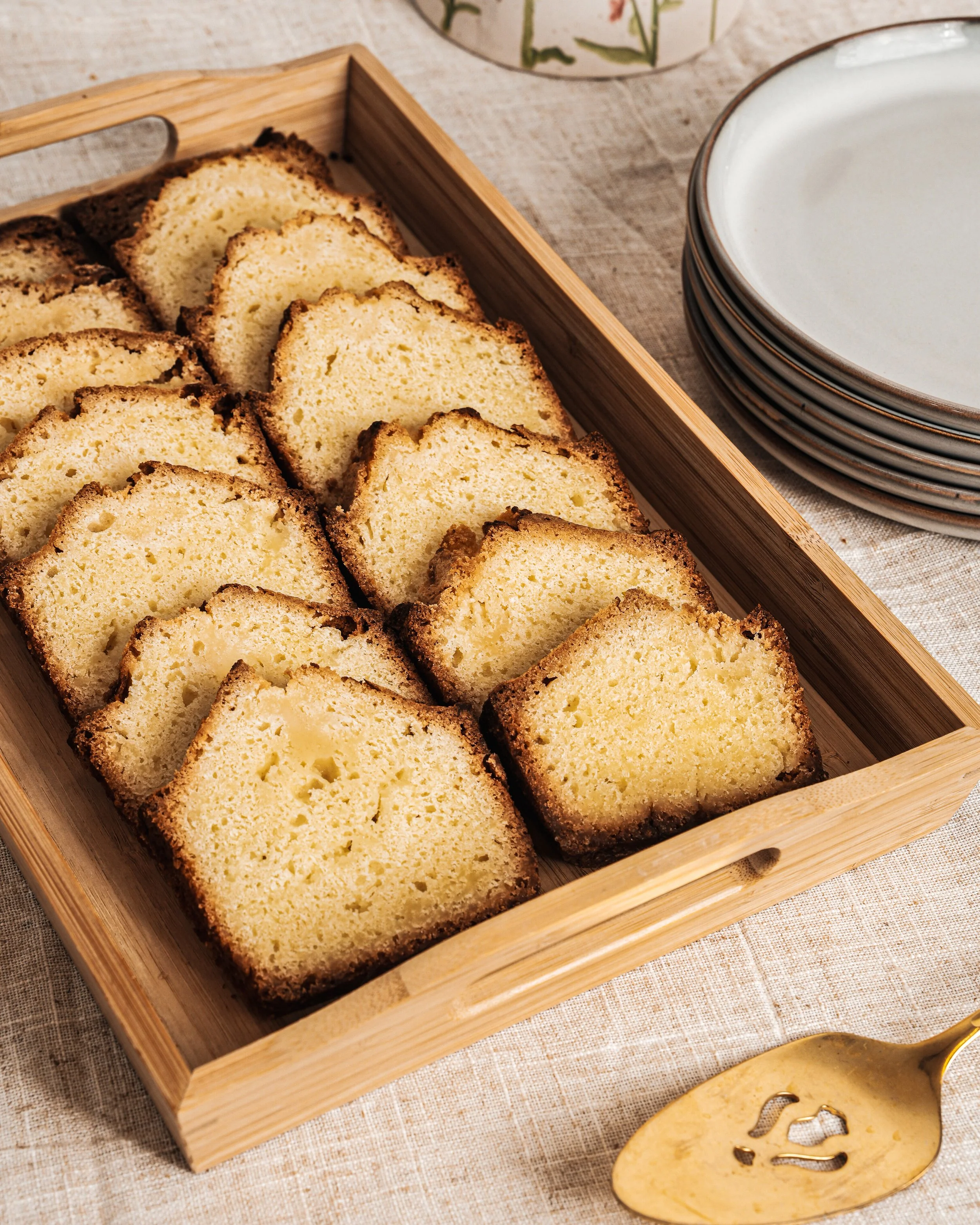 Tranches de gâteau dans un panier en bois, avec des assiettes empilées en arrière-plan et une cuillère en or en avant-plan.