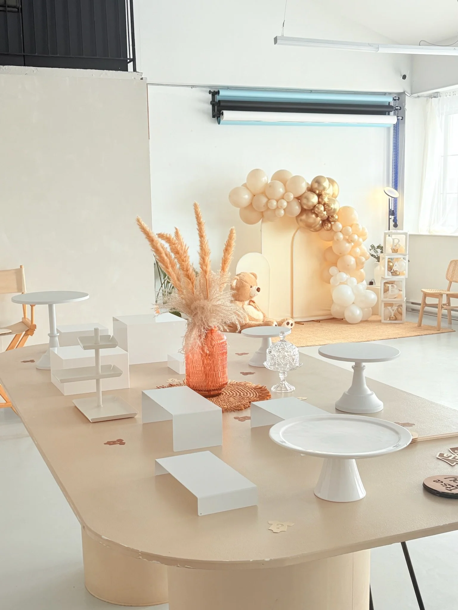 Décoration de fête avec un mur de ballons beige et or, poupée en peluche, vases avec végétation, et table avec plusieurs supports