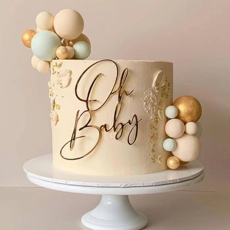 Gâteau blanc décoré avec des boules colorées en pastel et or, portant l'inscription 'Oh Baby' en script