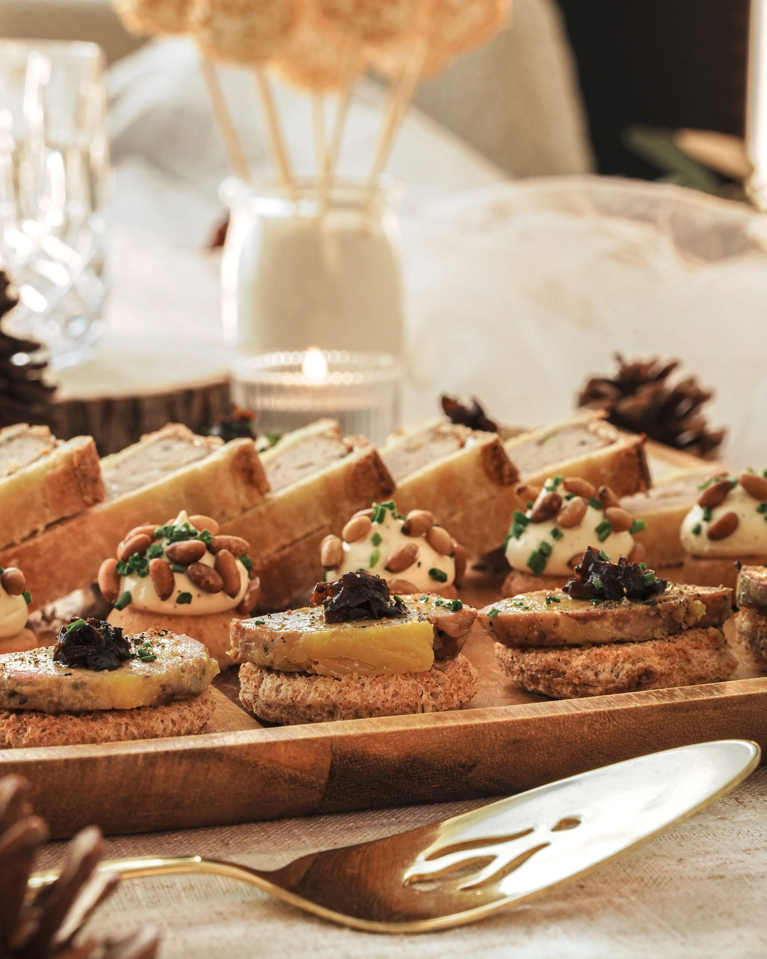 Assortiment de canapés et tapas décorés, avec un fond de décoration automnale comprenant des pommes de pin et des bougies.