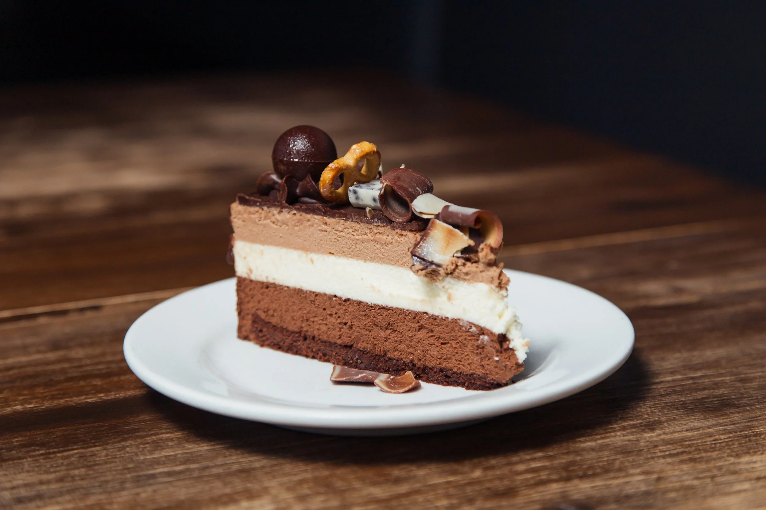 Part de gâteau chocolaté tranché sur une assiette blanche, avec trois couches de différentes textures et une décoration de chocolat et caramel en haut