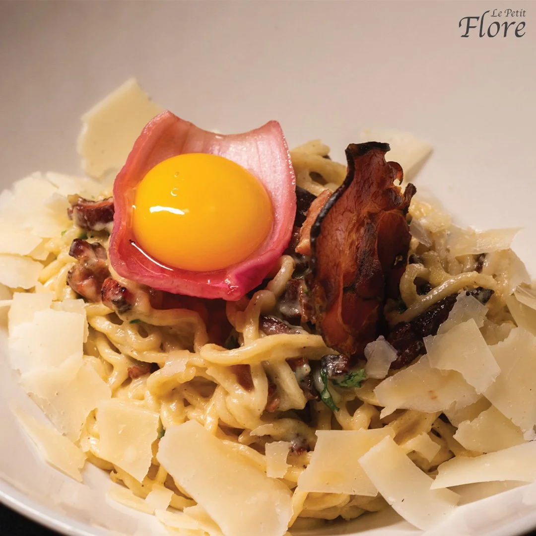 Plat de pâtes avec un œuf au plat, tranches de parmesan, bacon croustillant, champignons et herbes.