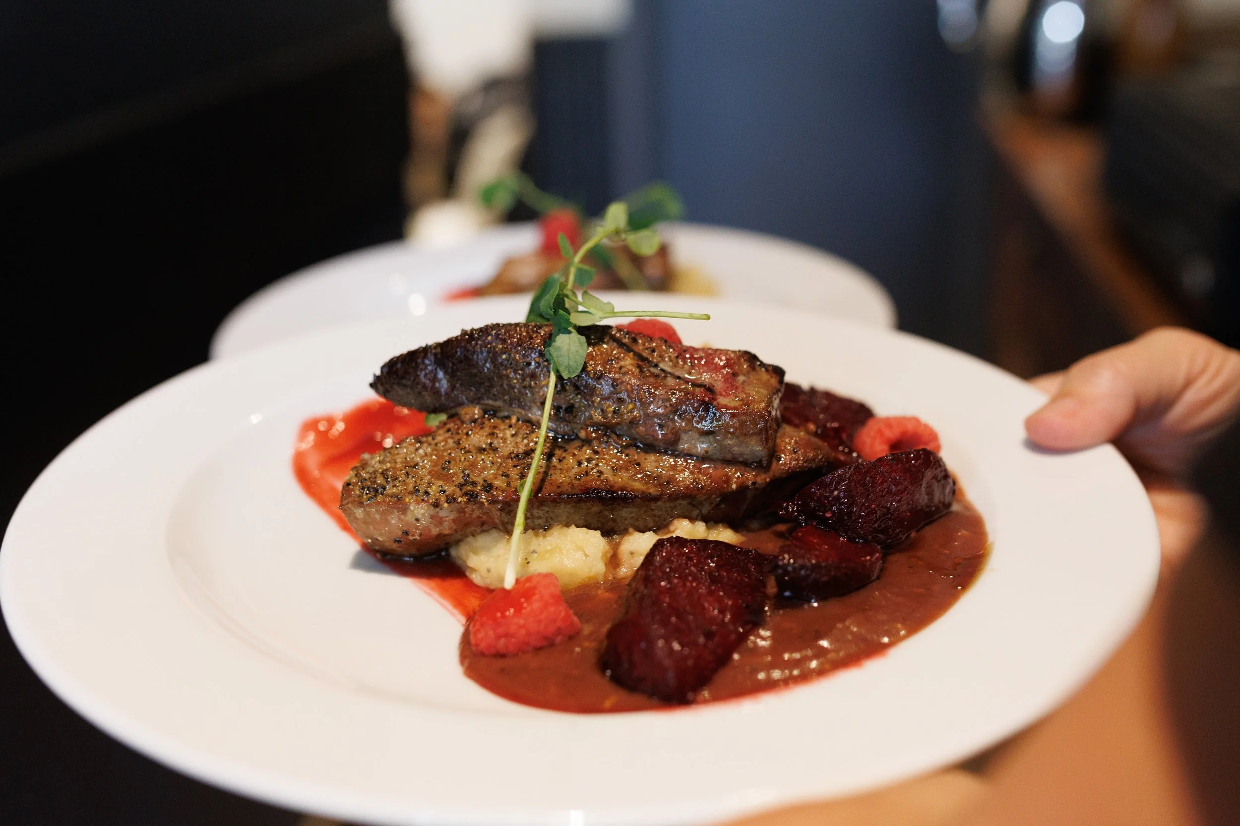 Assiette de viande avec sauce, légumes et purée, garnie d'une petite branche de herbes.