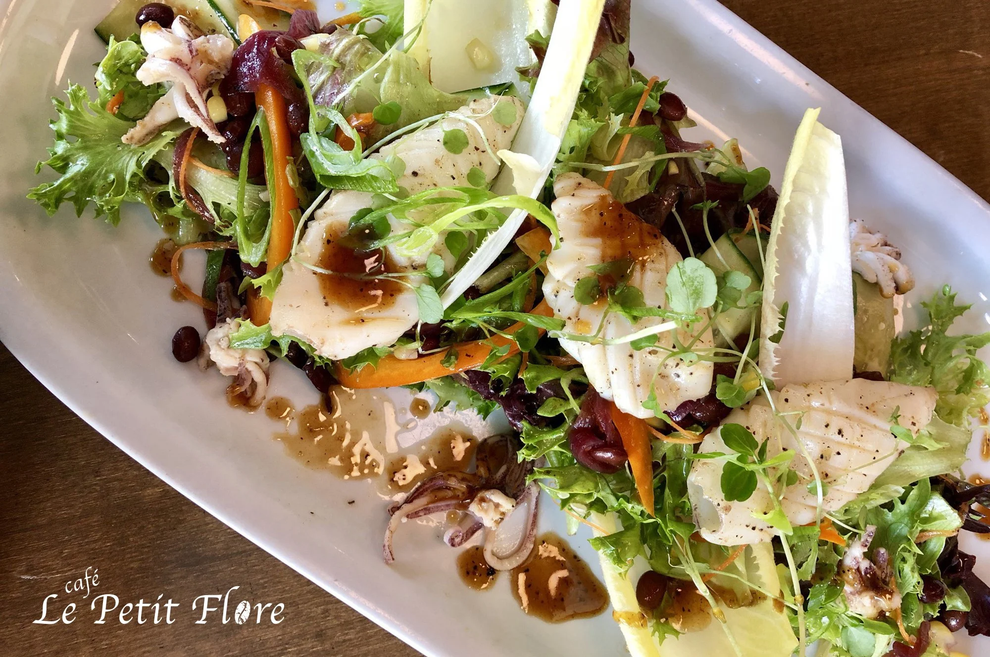 Salade de fruits de mer avec laitue, carottes râpées, micro-pousses, et vinaigrette sur une assiette blanche.