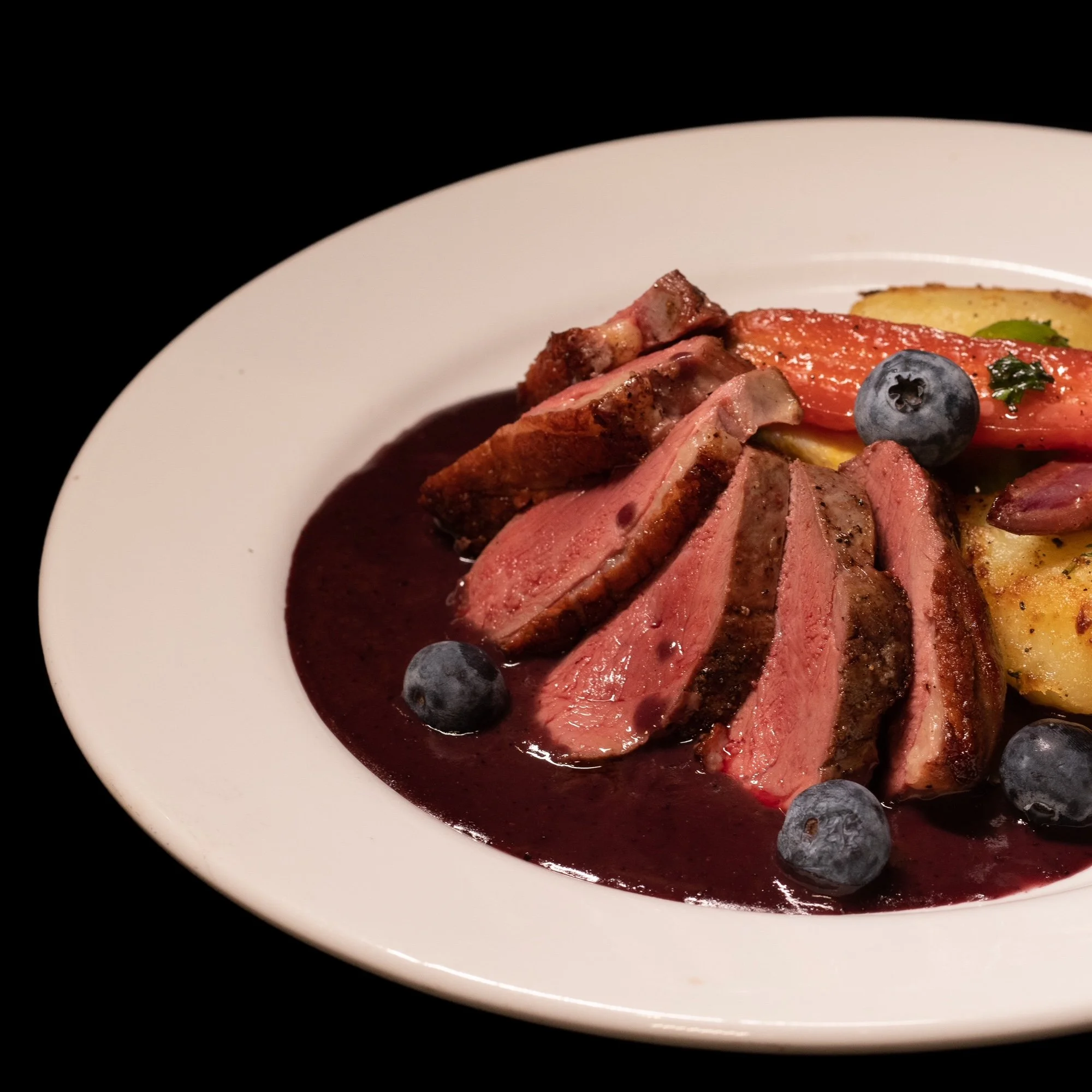 Assiette de filet de bœuf saignant avec sauce aux mûres, accompagnée de légumes grillés et de myrtilles.