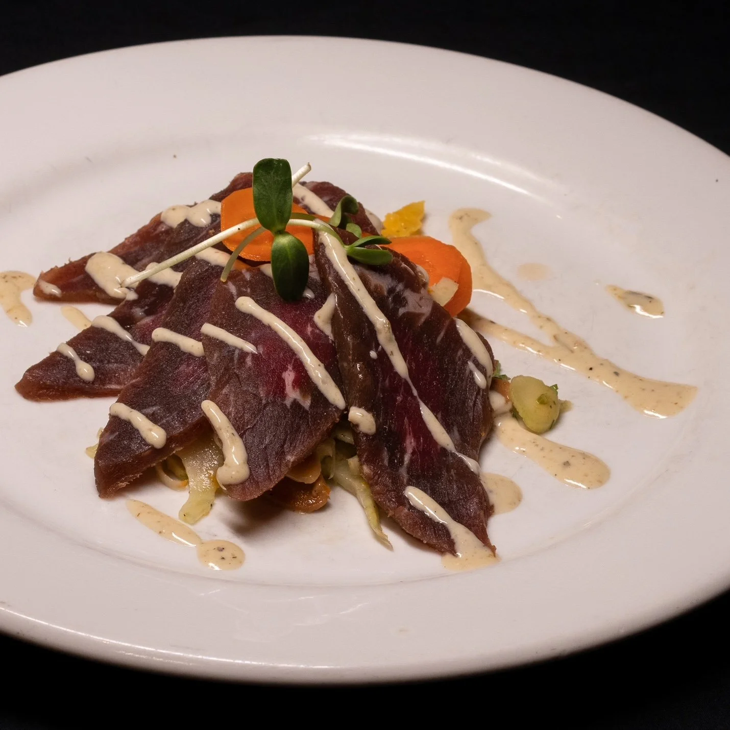 Tartare de bœuf avec de la sauce, garnitures de légumes et micro-pousses, présenté sur une assiette blanche.