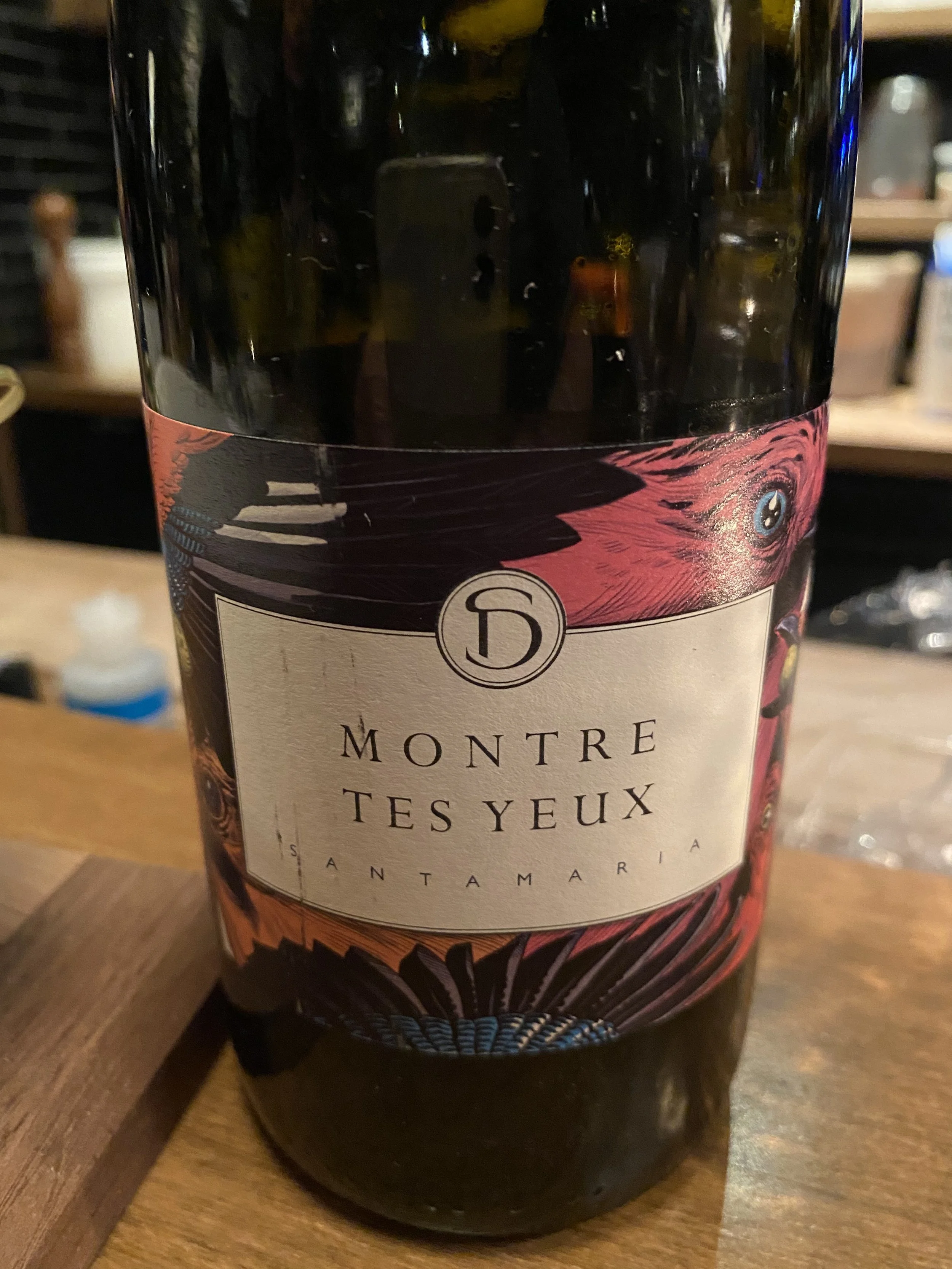 Bouteille de vin rouge avec une étiquette cardinal rouge et noire, portant le nom 'Montre Tes Yeux'.