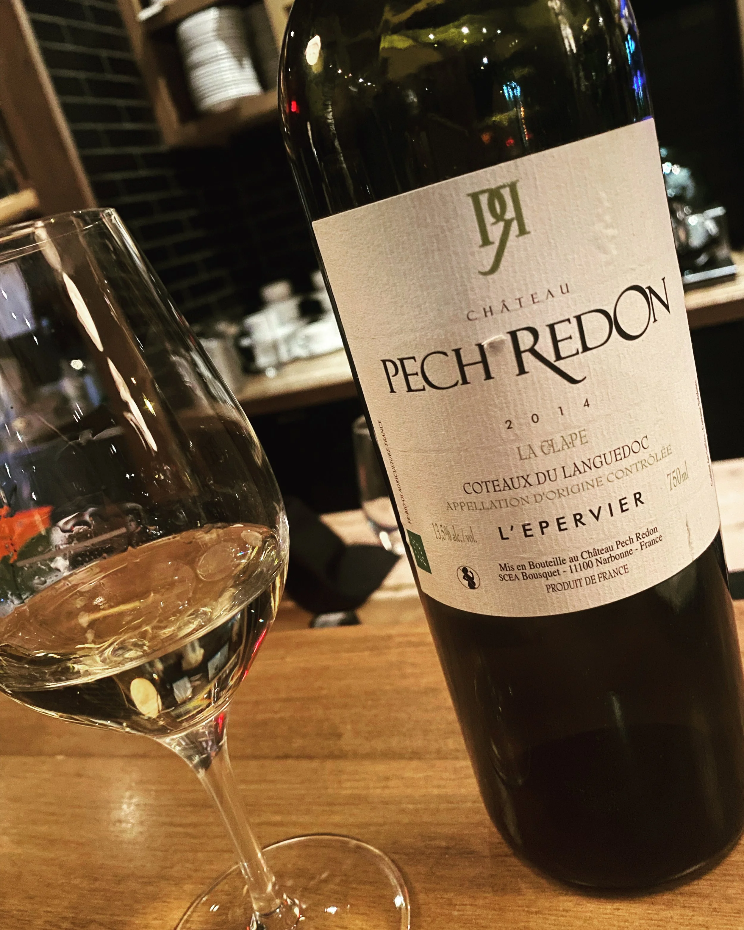 Bouteille de vin blanc Château Pech Redon et verre de vin blanc vide sur une table en bois