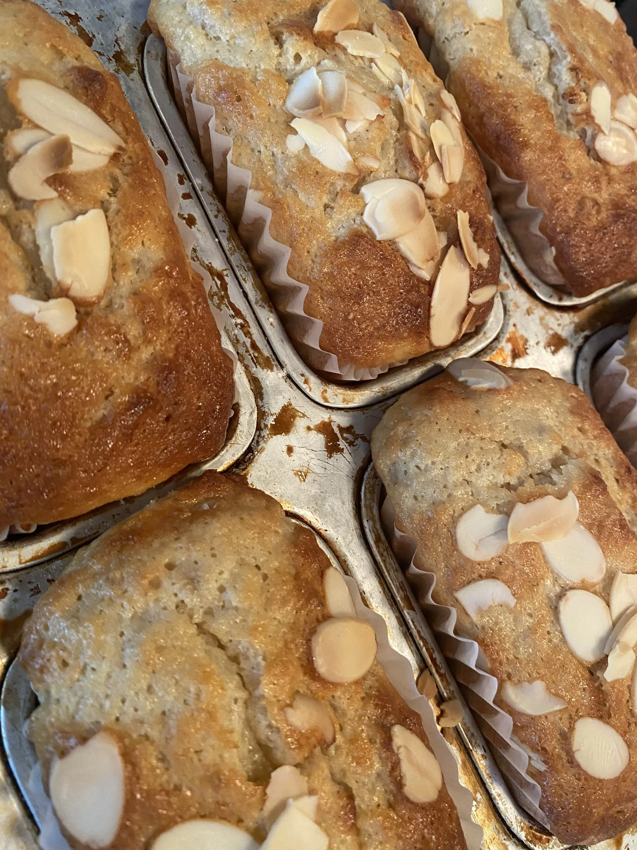 Muffins aux amandes fraîchement cuits, garnis de lamelles d'amandes, dans des moules en papier dans un moule à muffins.