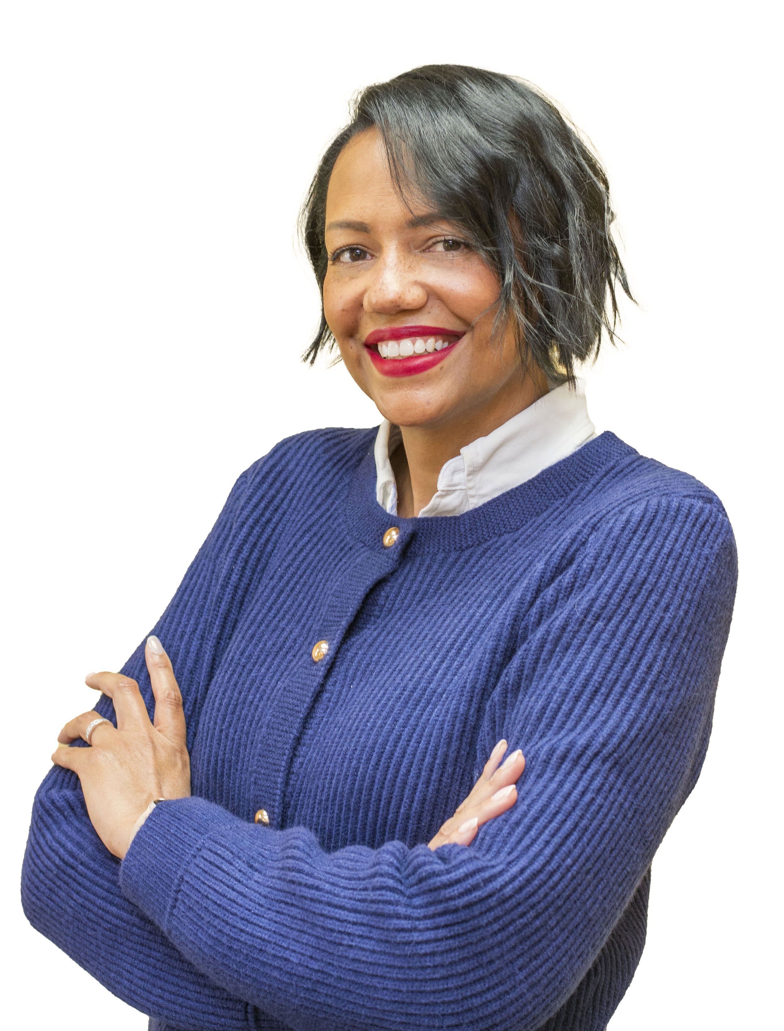 Portrait of a woman with long dark hair, wearing a blue blazer and gold buttons, smiling outdoors with a cloudy sky and water in the background.