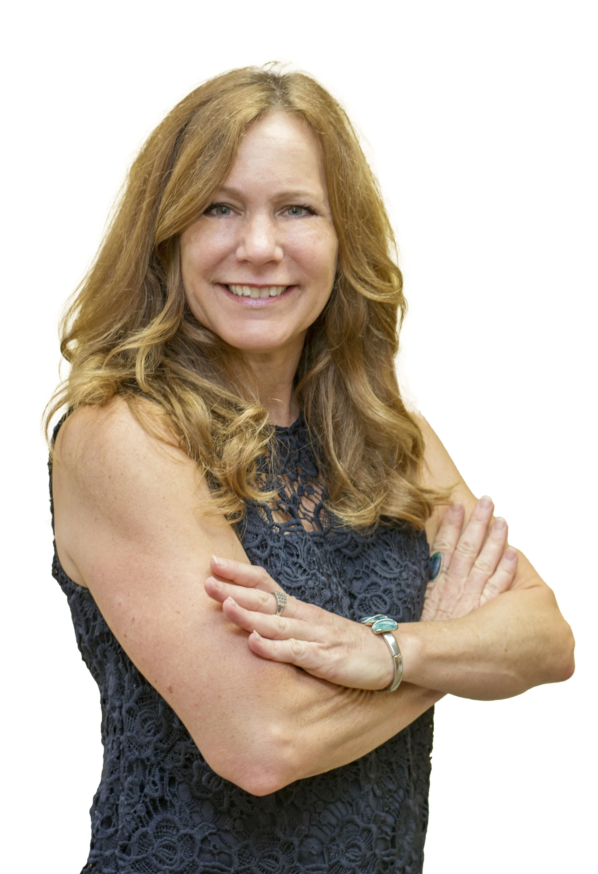A woman with blonde hair smiling and wearing a colorful, patterned sleeveless top, sitting indoors.