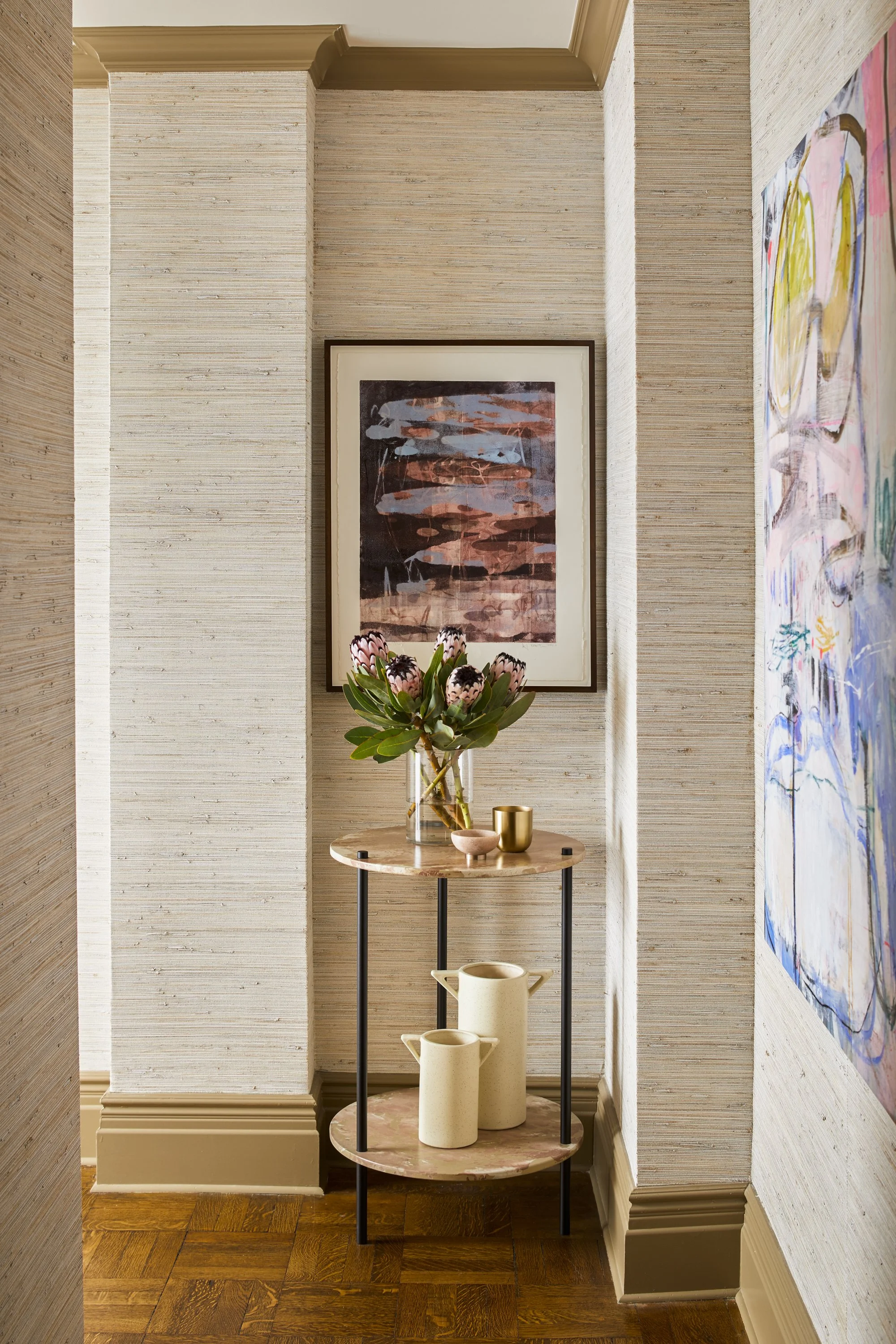 Corner with decorative table, abstract paintings, flower vase, and ceramic pitchers.