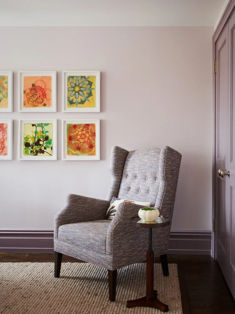Cozy room corner with a patterned armchair, small wooden side table, and abstract floral wall art.