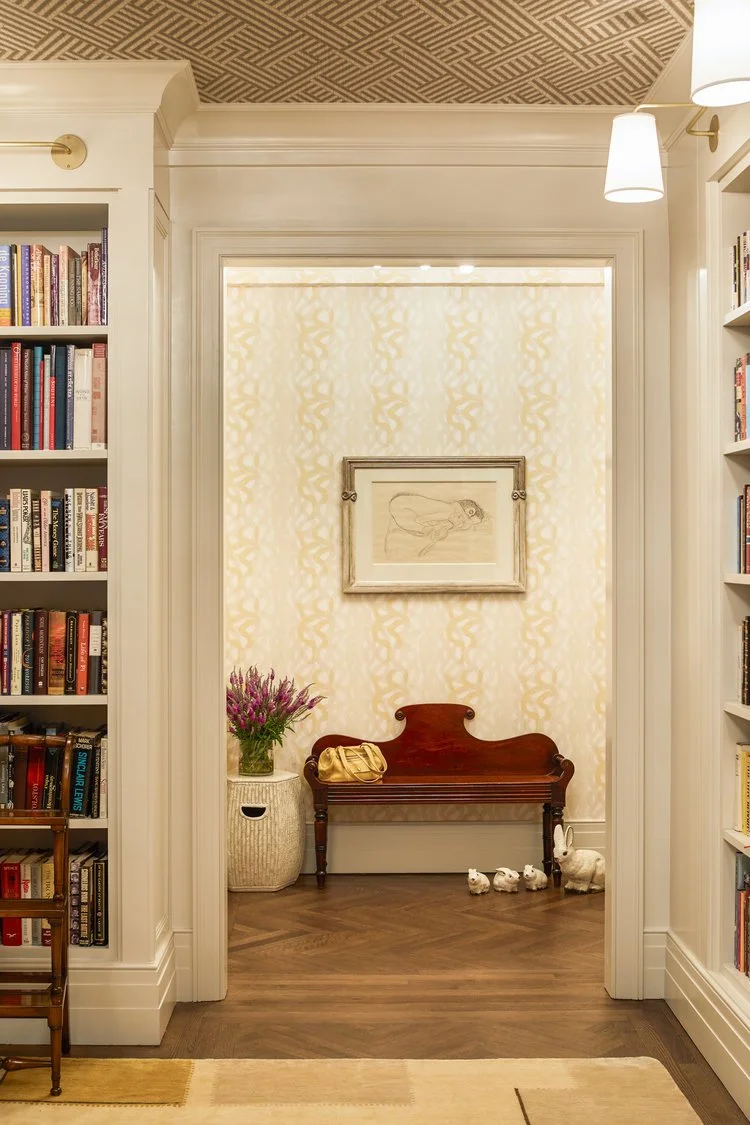 Interior hallway with bookshelves, wooden bench, artwork, decorative vase, and small animal figurines.
