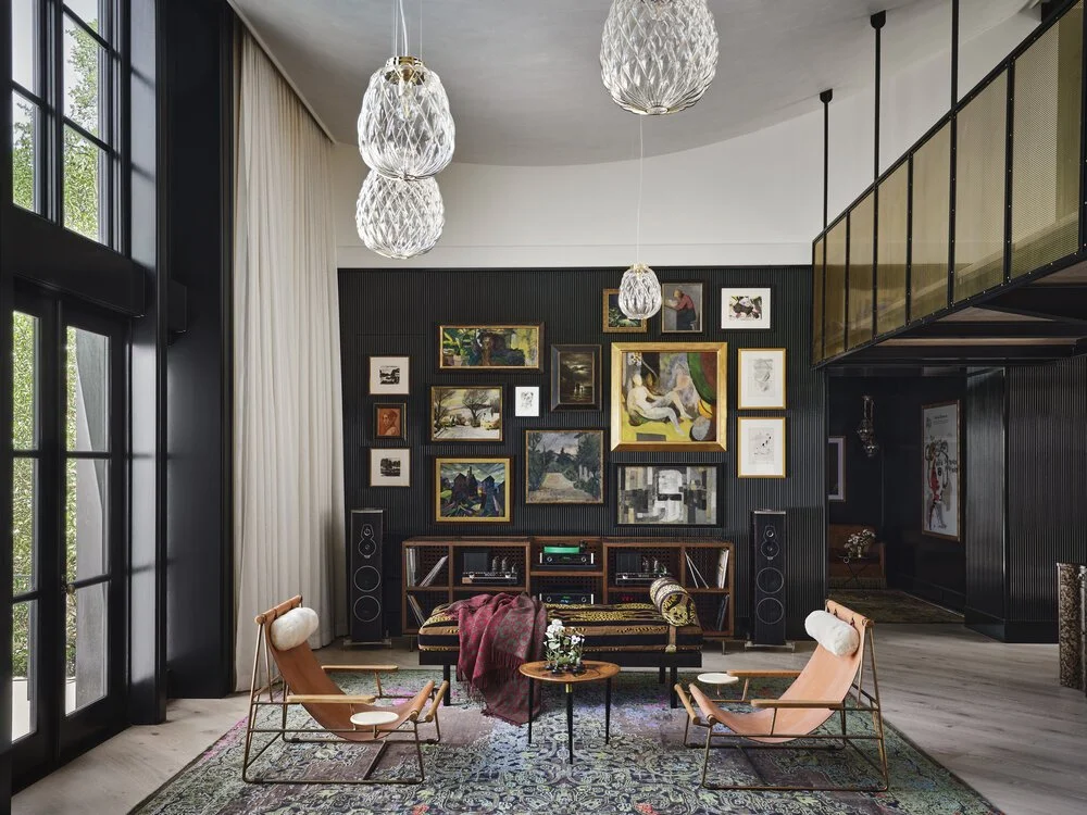 Stylish living room with art gallery wall, leather chairs, large windows, and modern lighting.