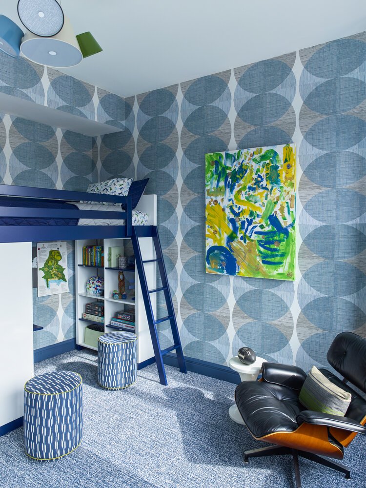 Modern children's room with blue and white geometric wallpaper, loft bed, bookshelf with toys, and colorful abstract painting.
