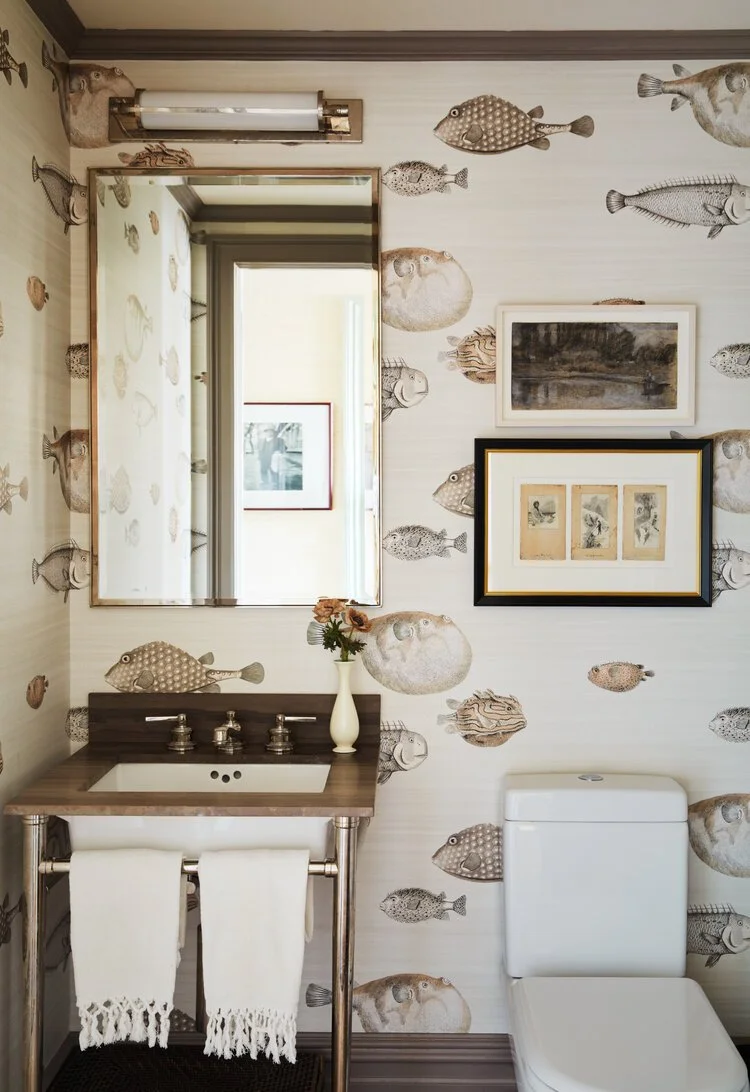 Bathroom with fish-themed wallpaper, framed art, sink, mirror, vase with flowers, and a toilet.
