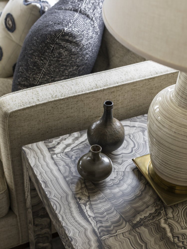 Close-up of a textured side table topped with small ceramic vases and a large table lamp beside a sofa with decorative pillows.