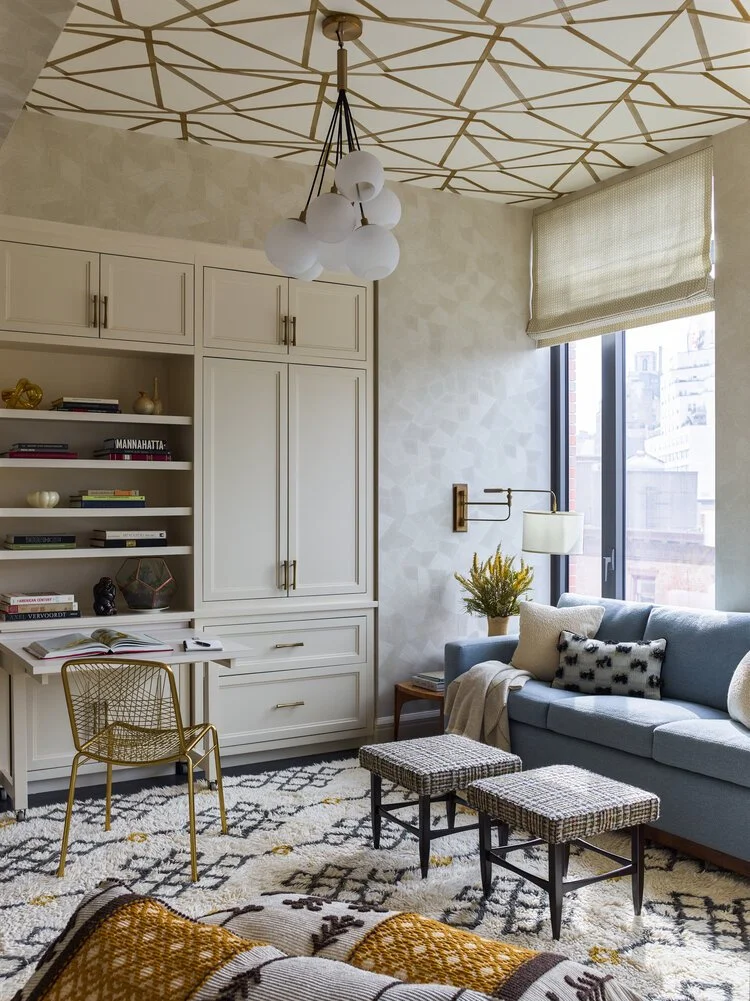 Modern living room with geometric ceiling design, blue sofa, patterned rug, built-in shelves, and a chandelier.