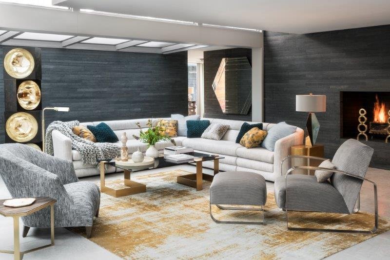 Modern living room with gray and white furniture, a sectional sofa, two armchairs, a fireplace, and decorative cushions. The room features a large rug, a coffee table, wall art, and contemporary lighting.