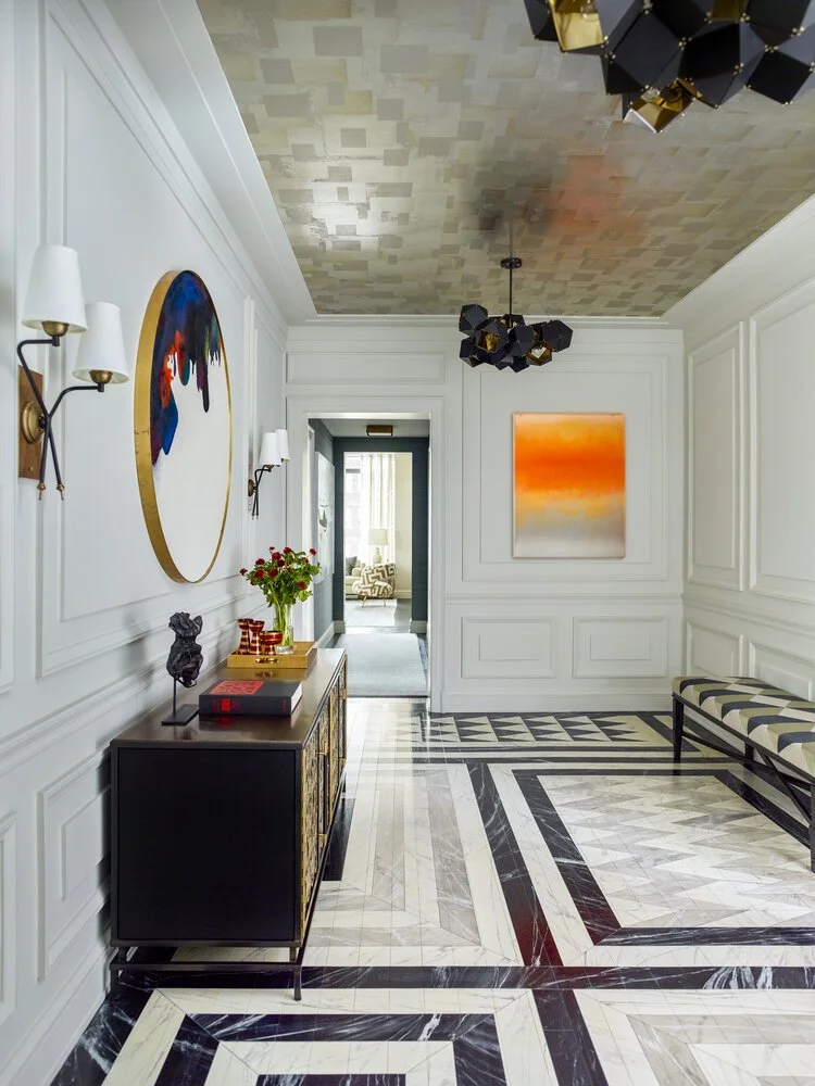 Elegant modern hallway with geometric flooring, abstract wall art, a black console table, decorative sculptures, and overhead lighting.