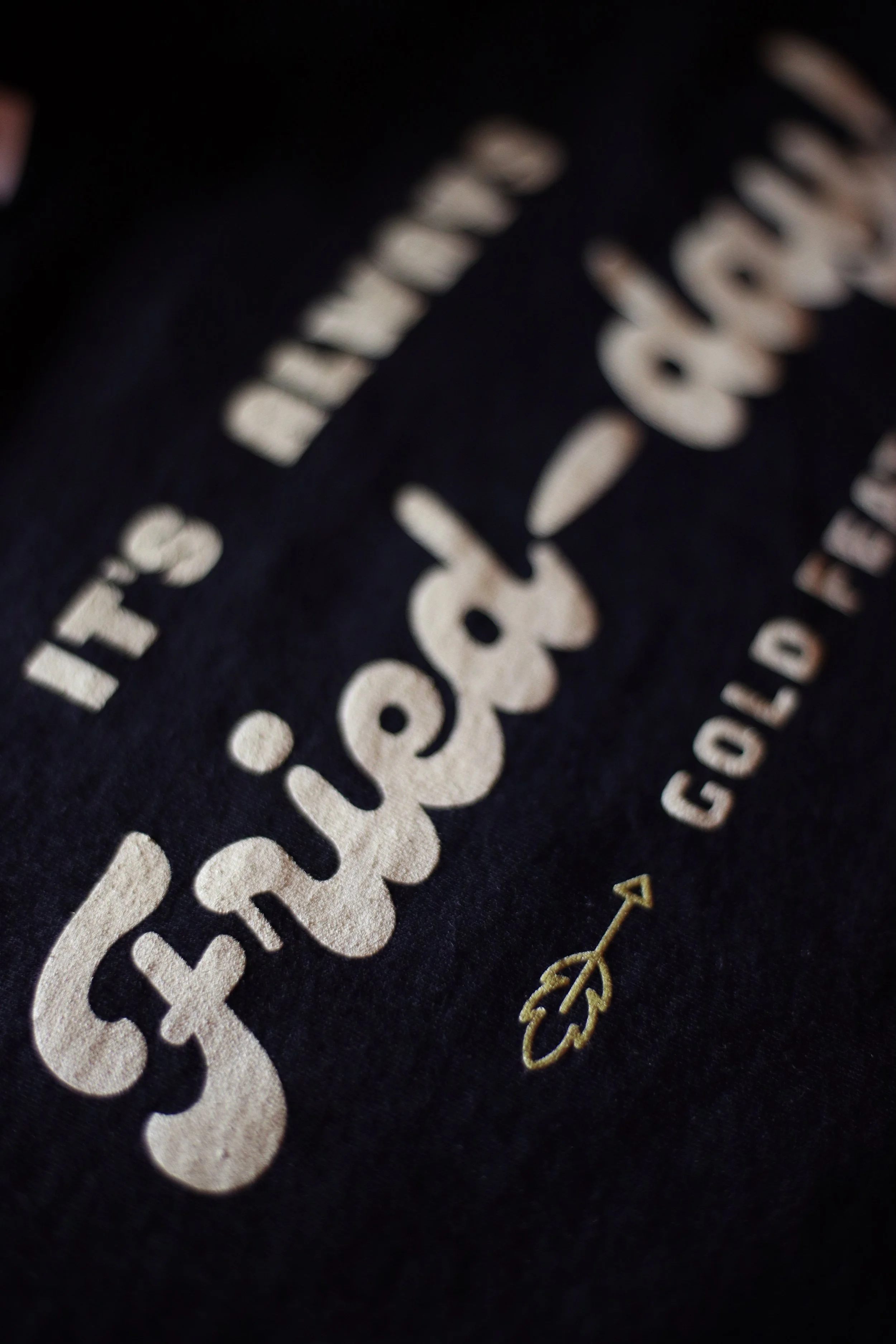 Close-up of a black fabric with white and gold embroidered text and a small design element.