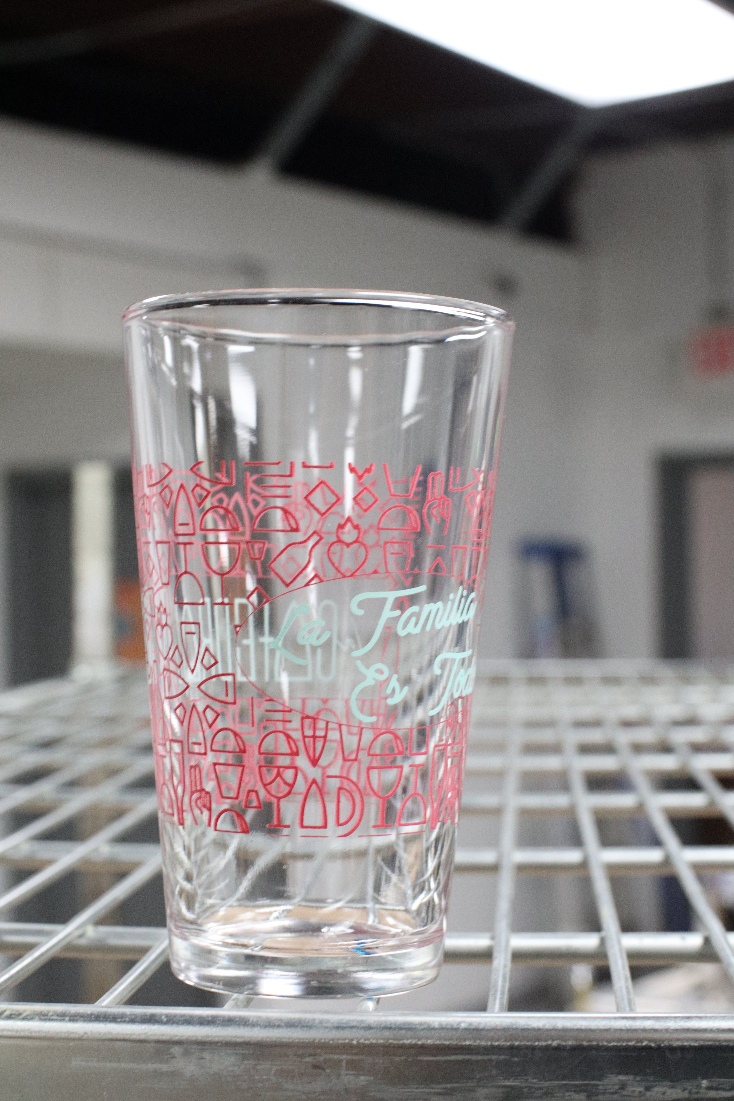 A clear glass with red decorative writing and patterns, placed on a wire shelf inside a refrigerator.