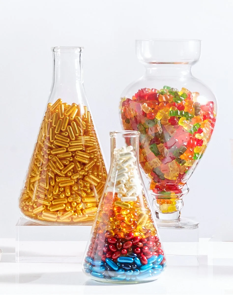 Three glass containers filled with colorful candies and capsules on a white surface.