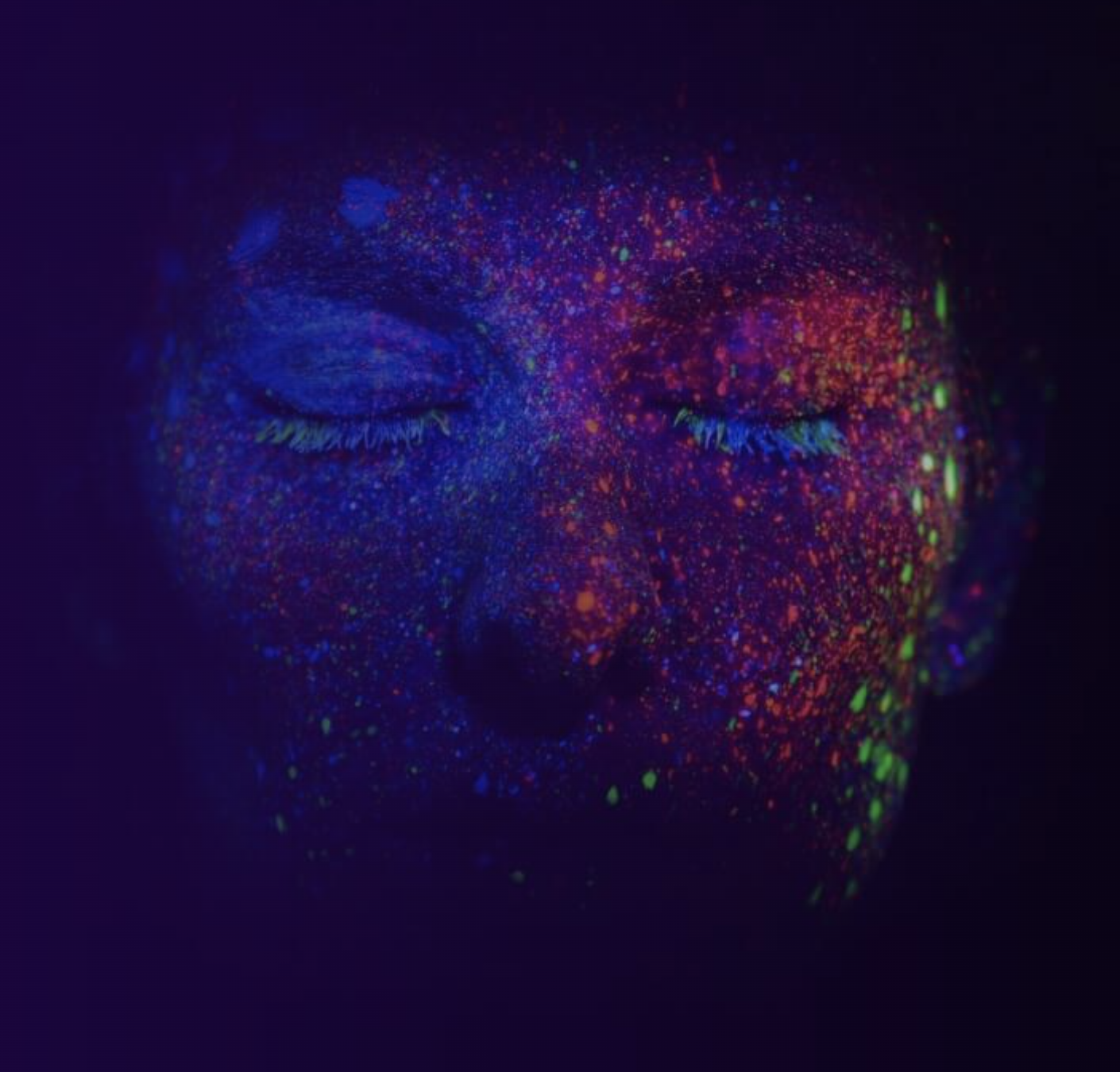 Close-up of a person's face with closed eyes, covered in fluorescent paint splatters in blue, red, green, and yellow under blacklight.
