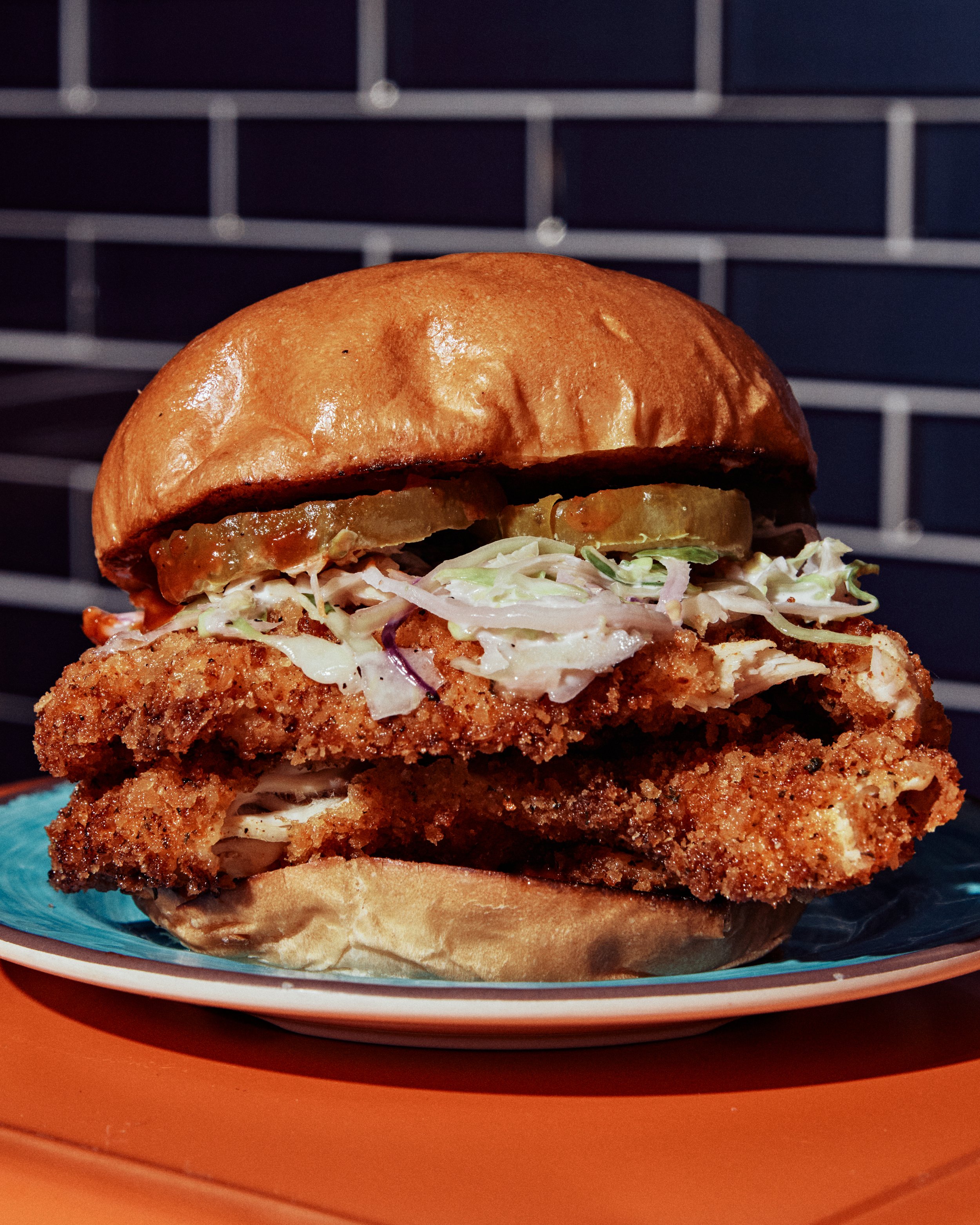 Close-up of a fried chicken sandwich with shredded lettuce, tomato slices, and sauce inside a toasted bun, served on a colorful plate.