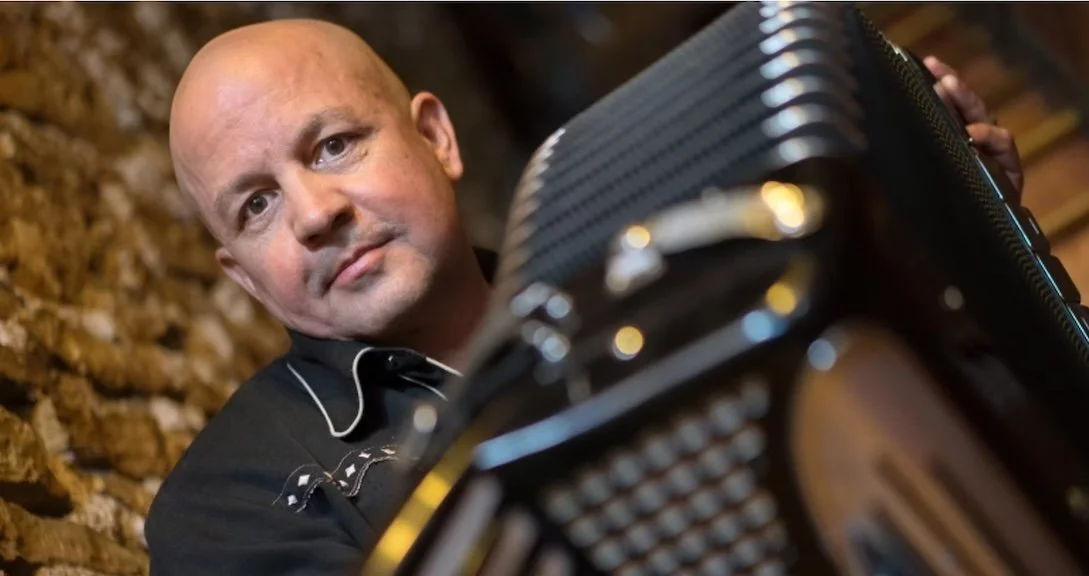 man looks over the edge of an accordion he is playing