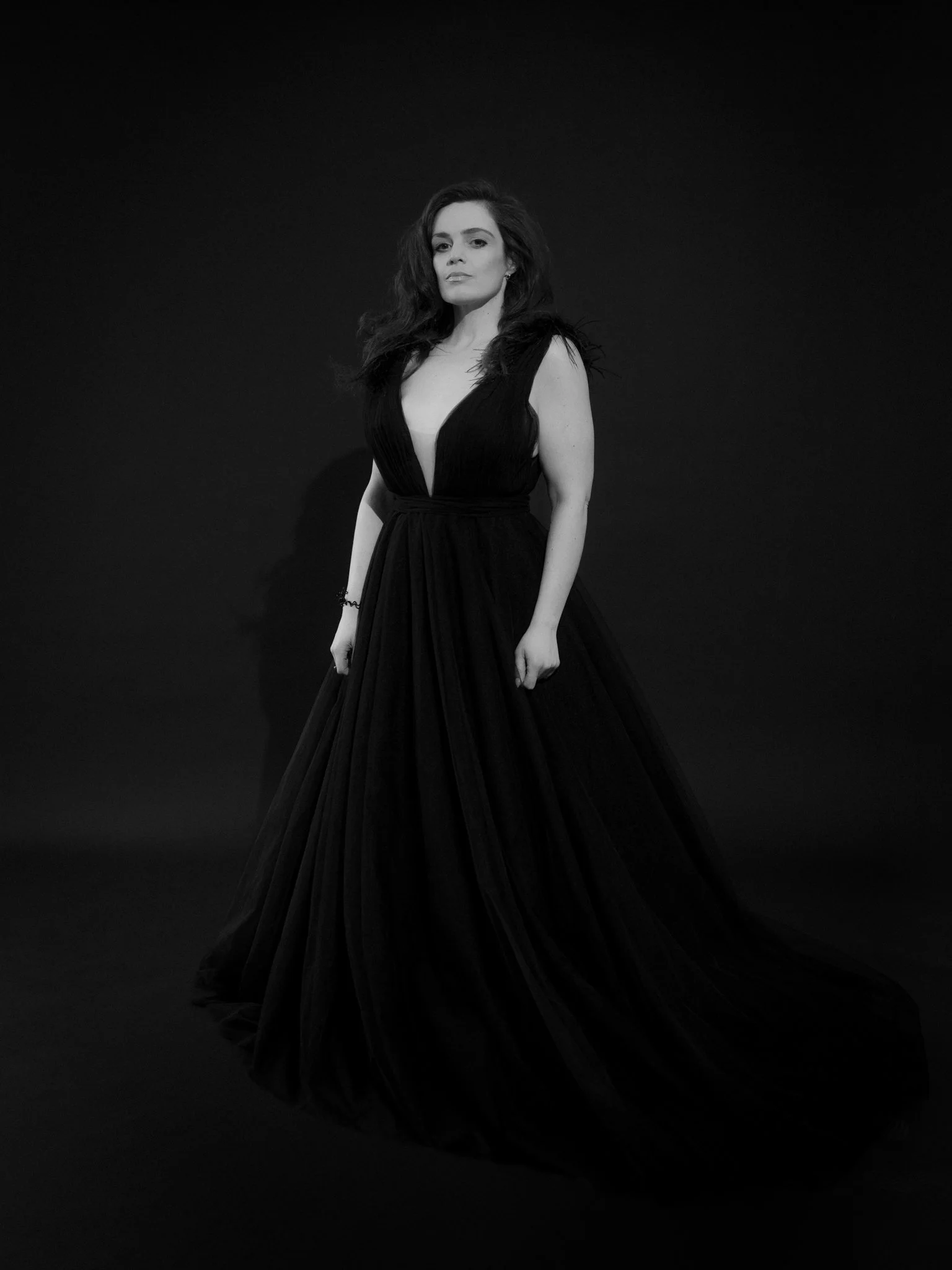 A woman in a long, black elegant gown standing against a dark background.