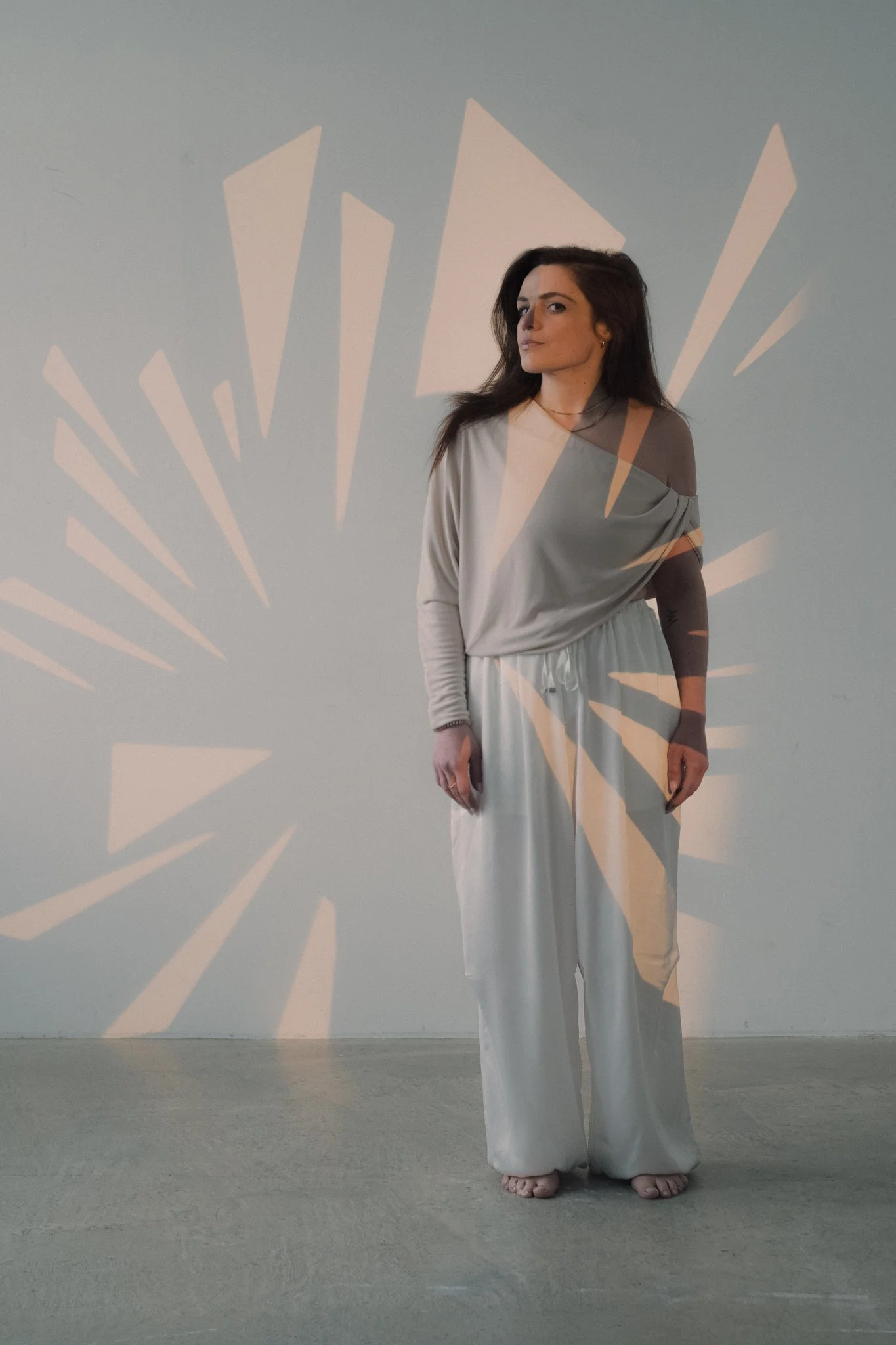 A woman standing against a plain wall with light projections creating abstract patterns around her.