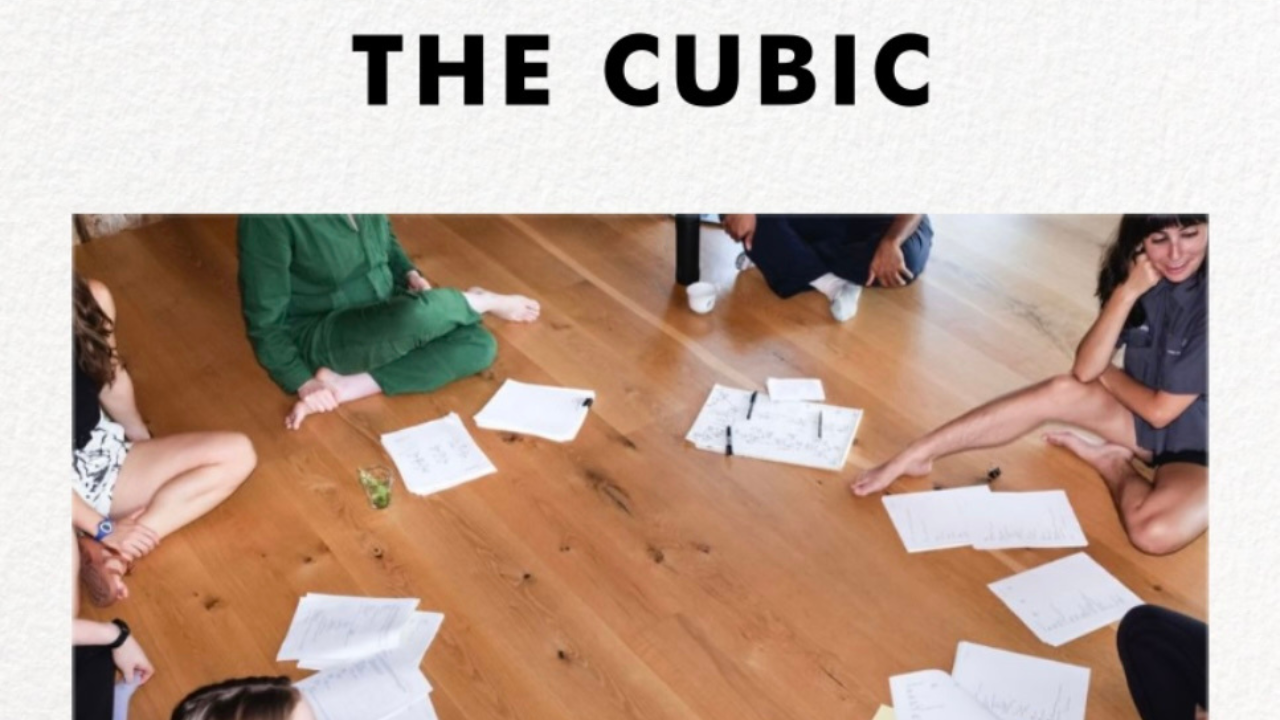 The Cubic with people sitting in a circle on a wooden floor with scripts in front of them
