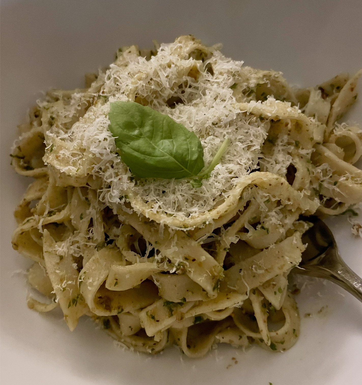 Image of pasta with pesto, cheese, and a basil leaf on top.