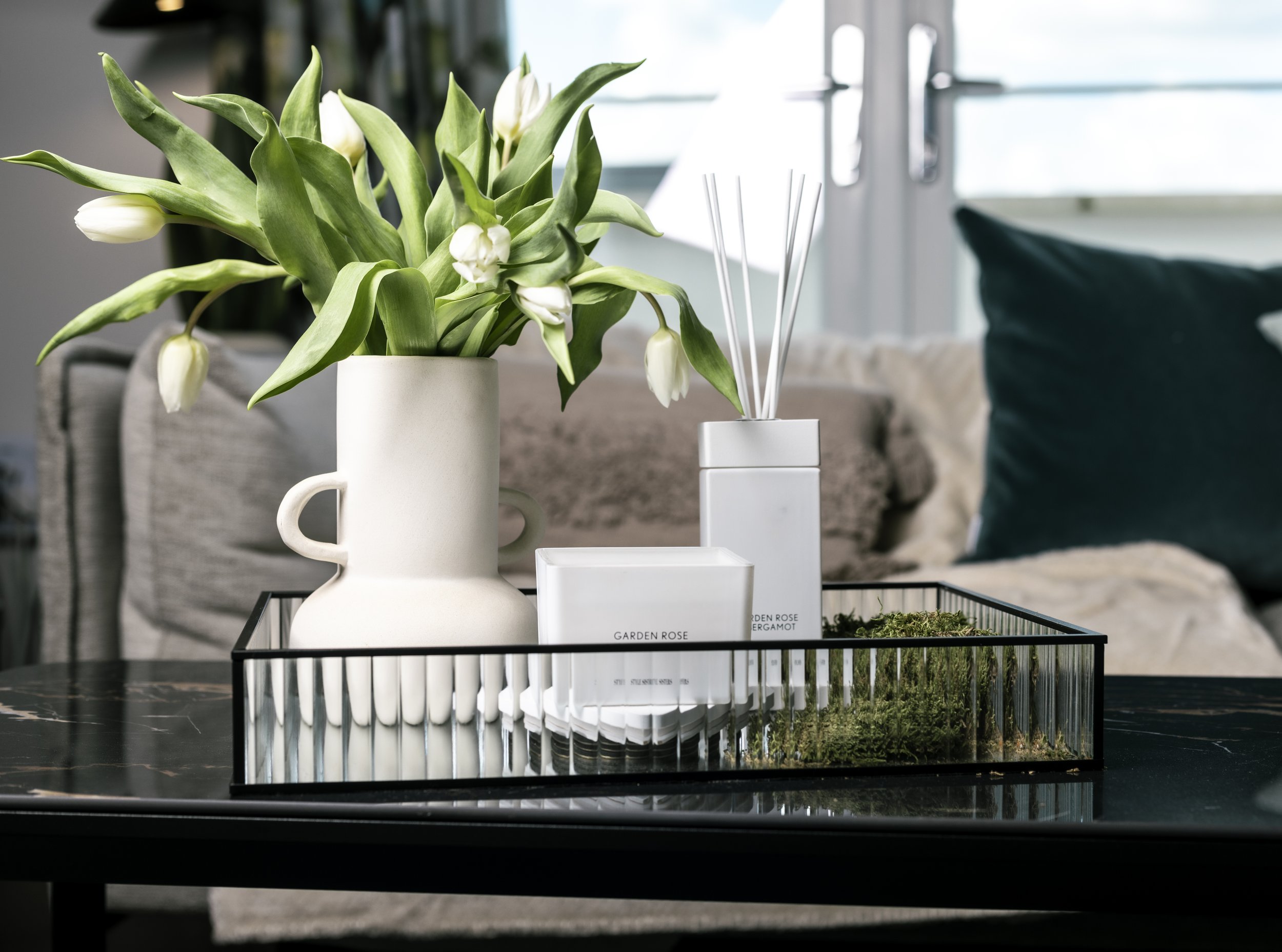 White vase with tulips on tray with scented candle and diffuser on dark table, modern cozy room.