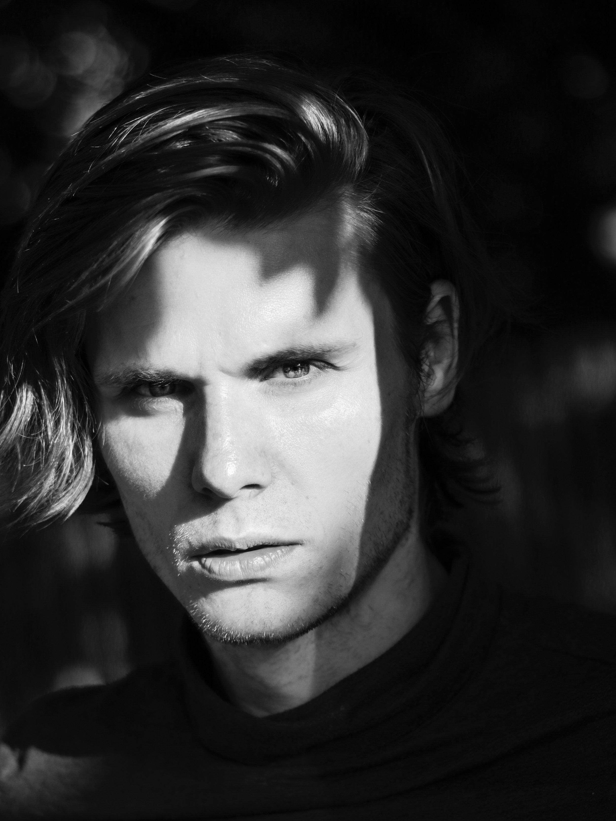 Black and white portrait of a person with long hair and serious expression, partially shaded.