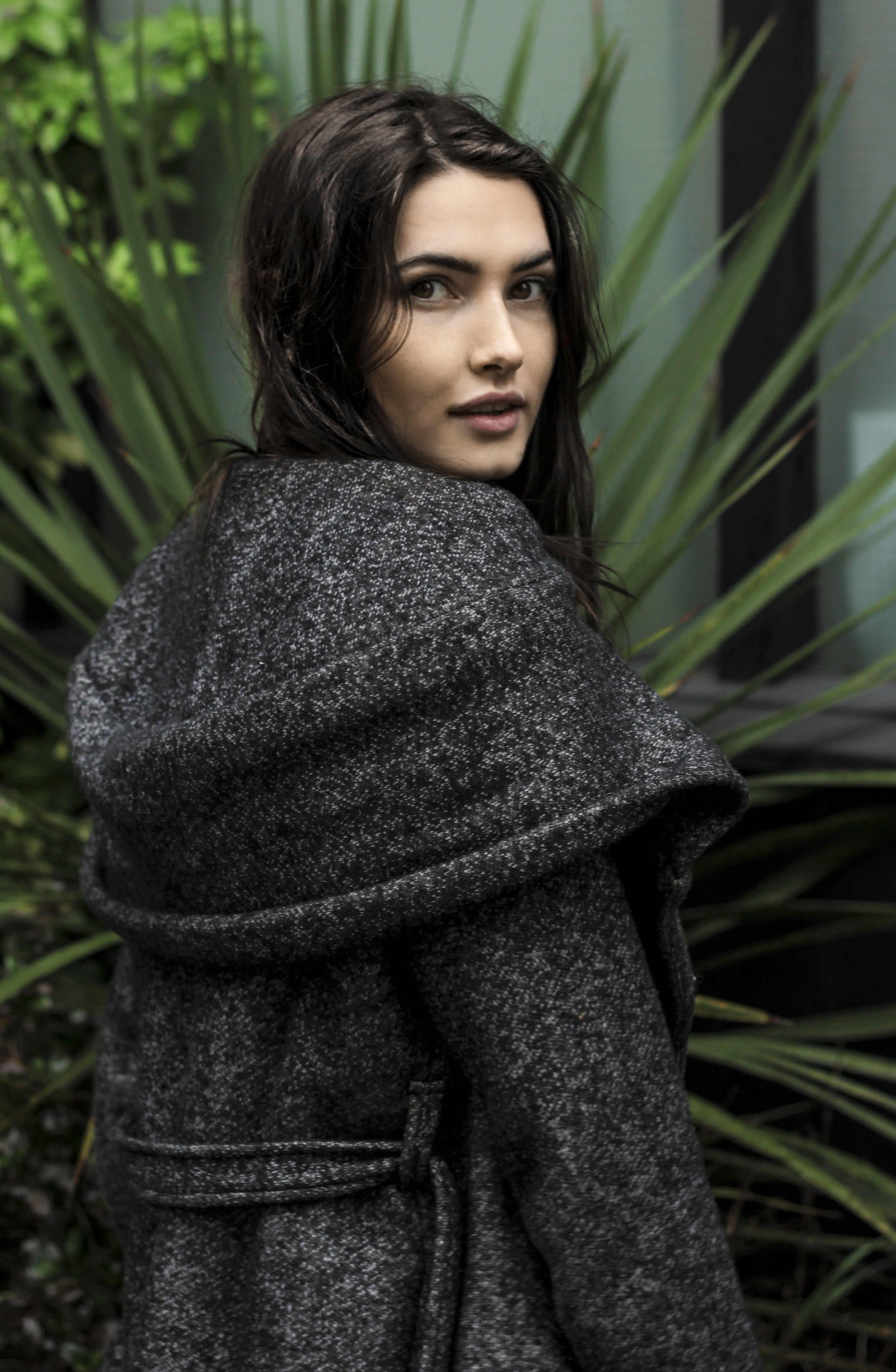 Woman in gray coat standing in front of greenery