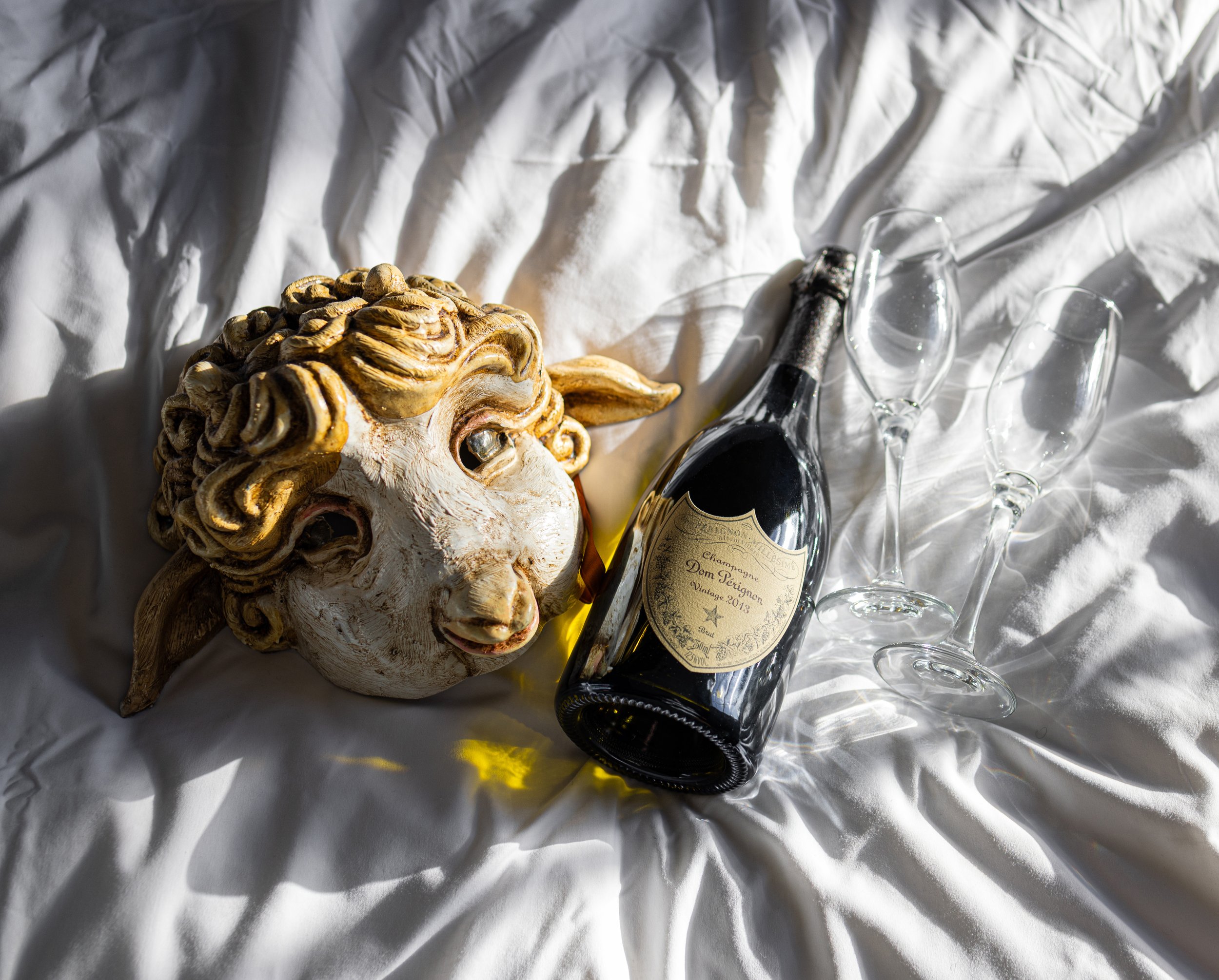 Champagne bottle with sheep mask and glasses on white fabric