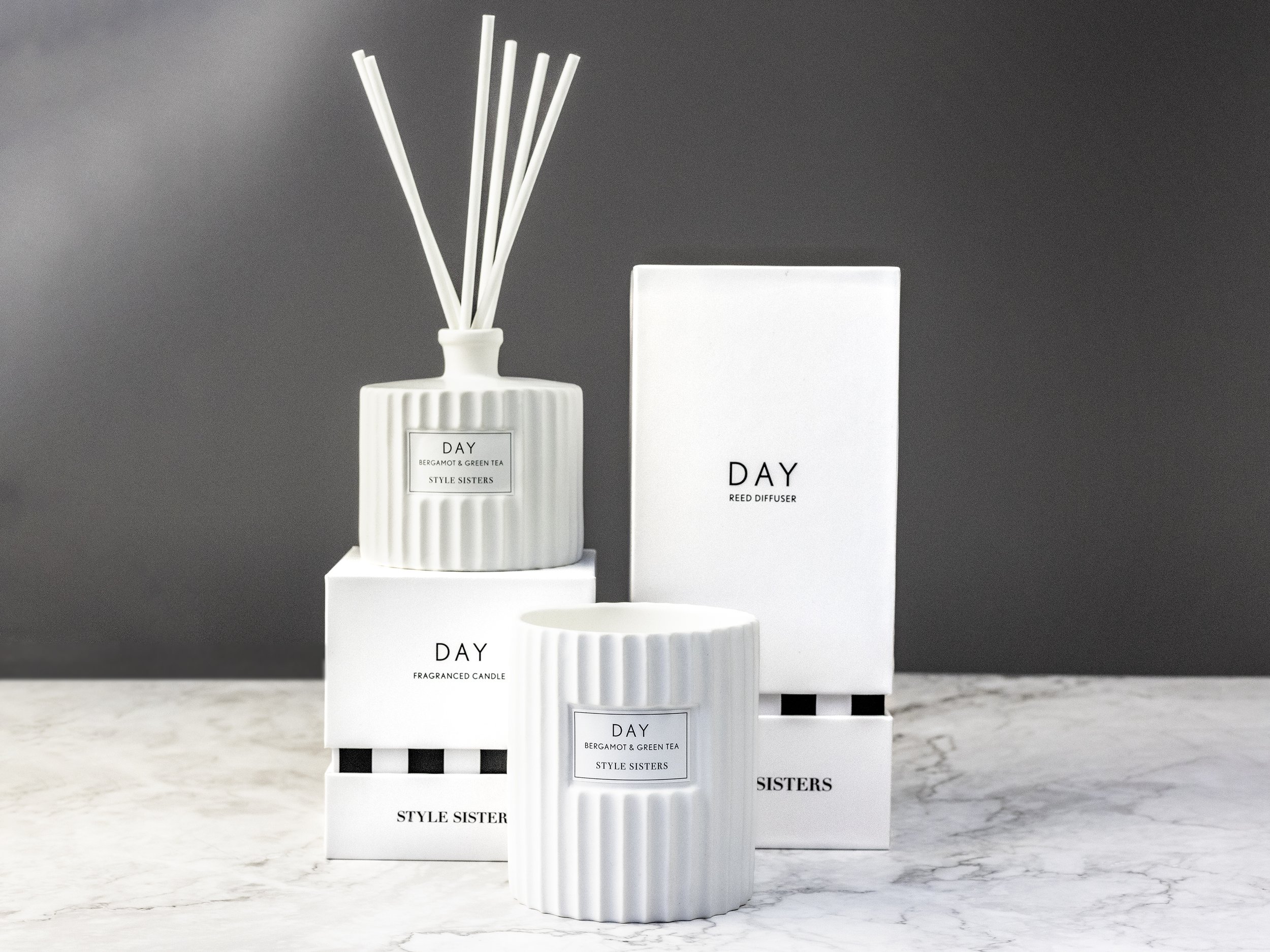 Reed diffuser and candle with packaging on a marble surface
