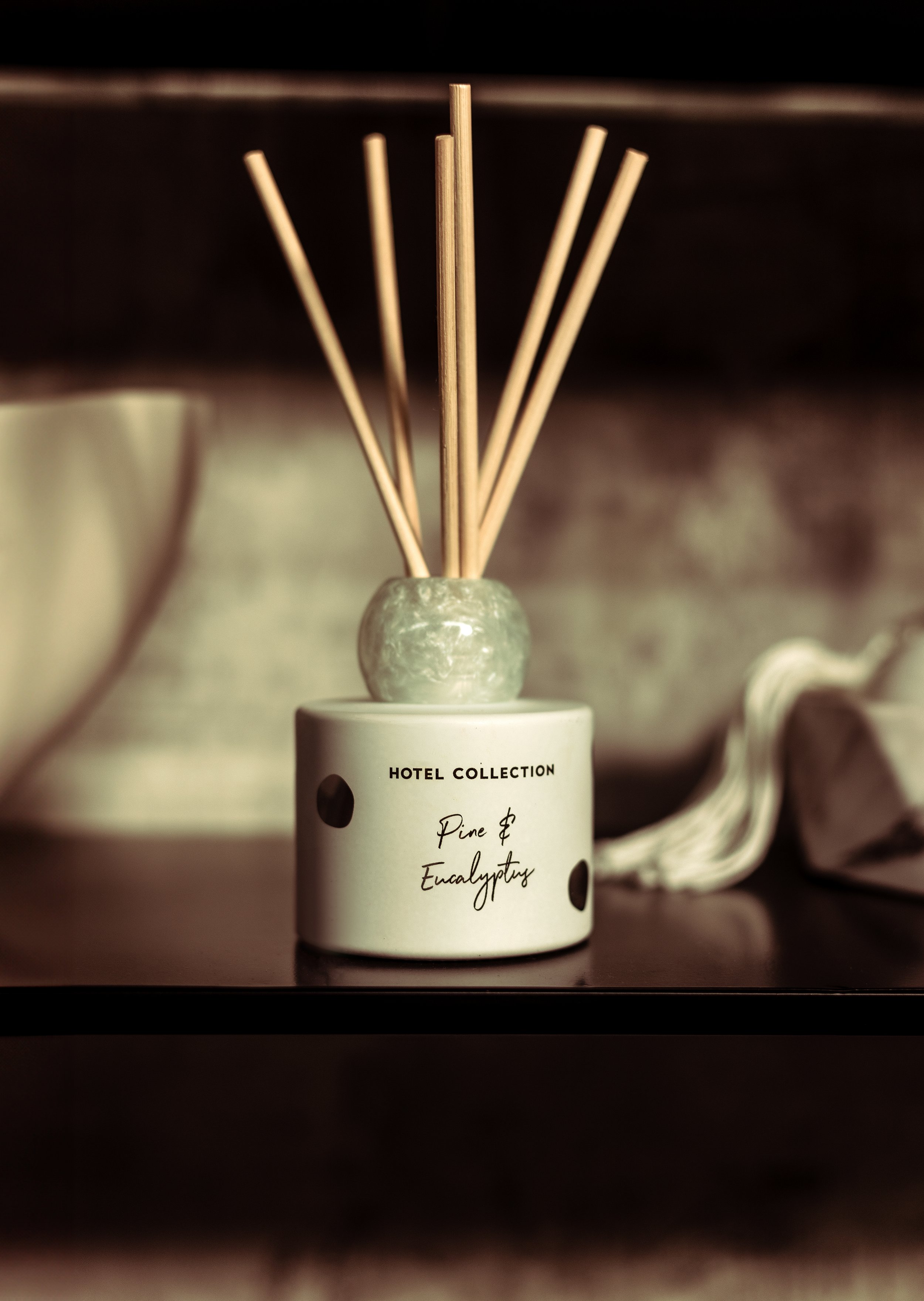Aromatic reed diffuser labeled 'Hotel Collection Pine & Eucalyptus' with wooden sticks in a ceramic container.