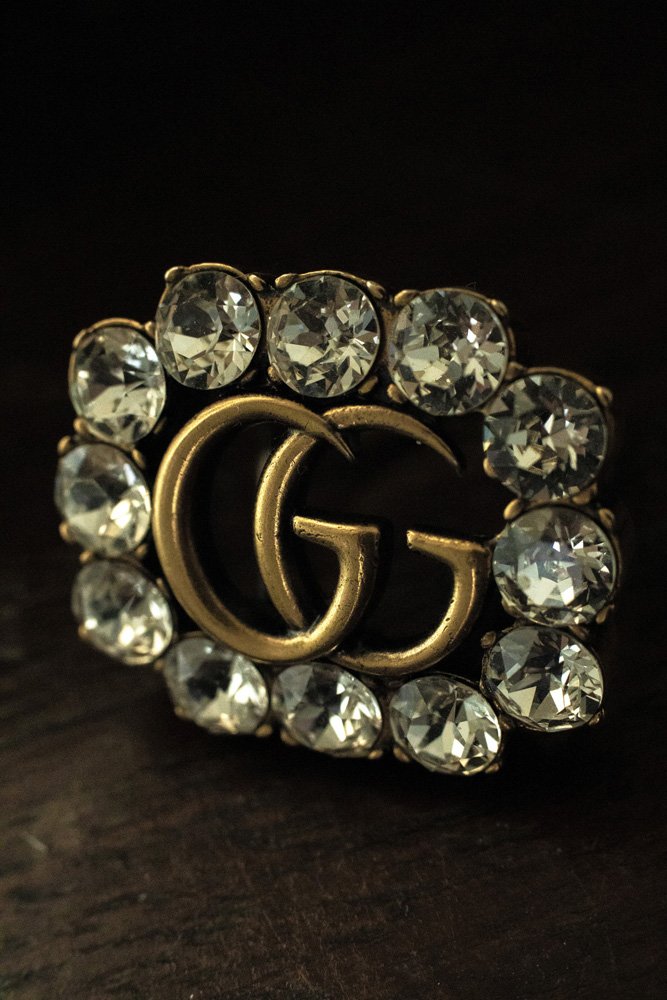 Close-up of a decorative buckle with rhinestones and interlocking "GG" letters on a dark background.
