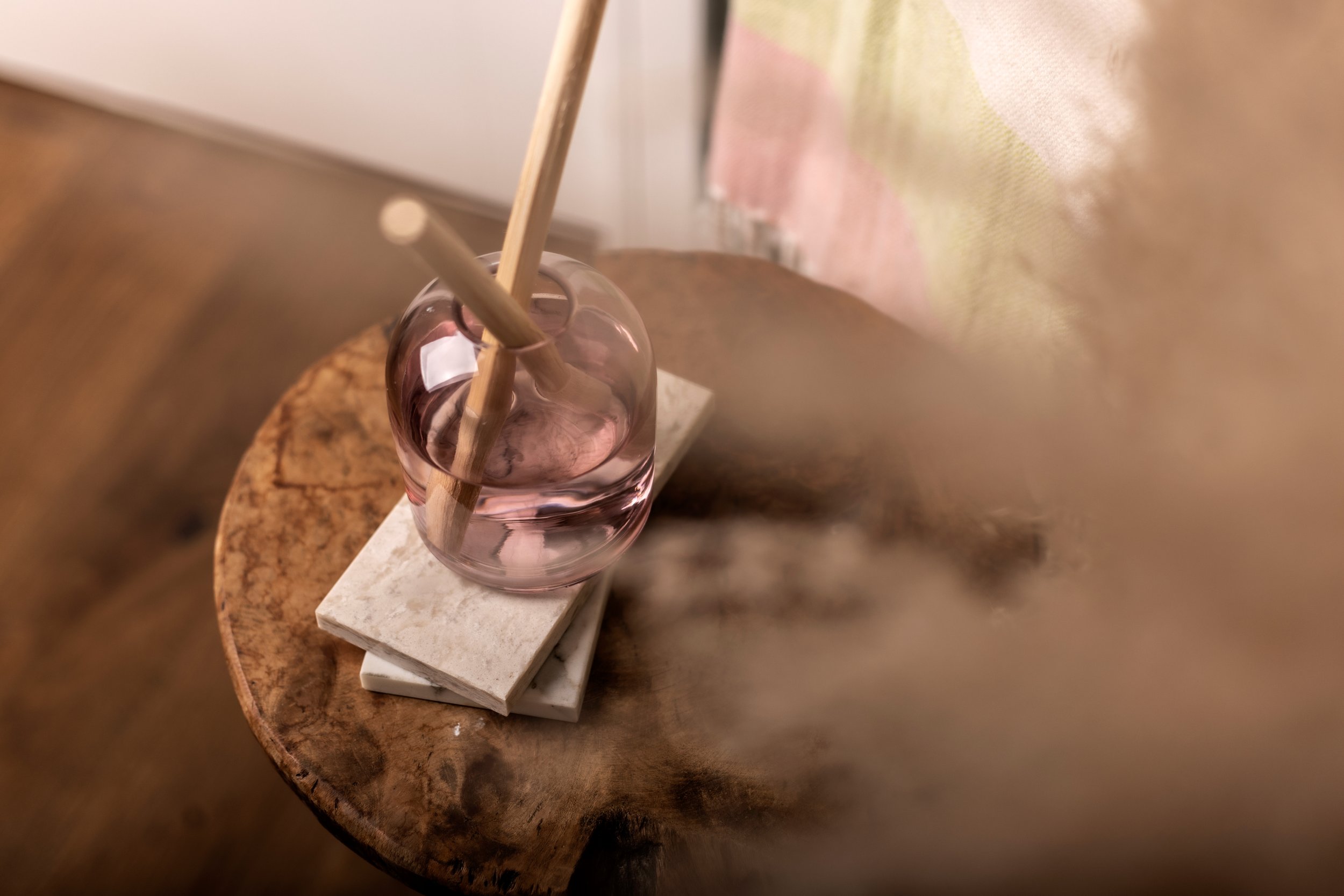 Pink glass diffuser with wooden reeds on a wooden table.