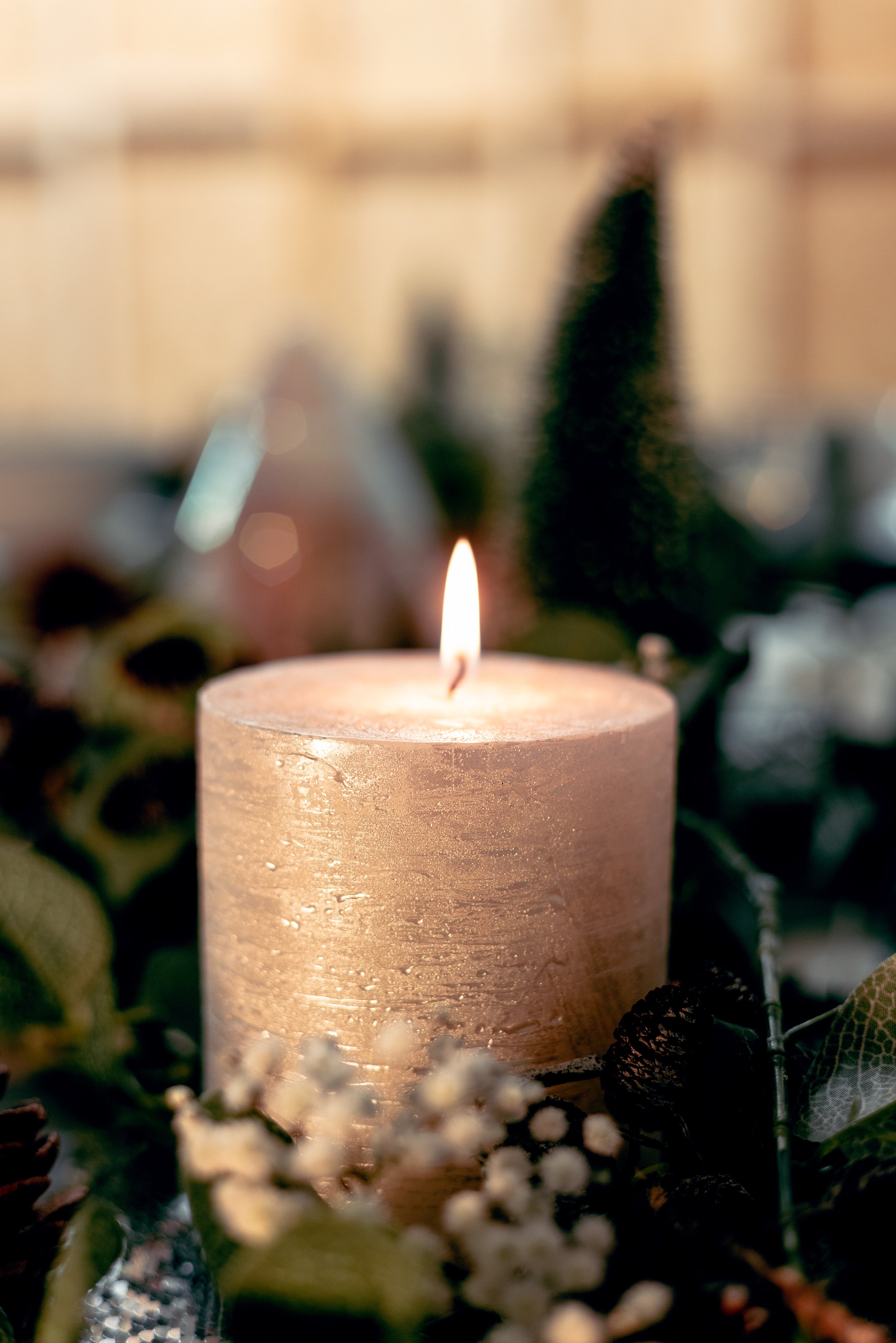 Lit candle surrounded by greenery and flowers