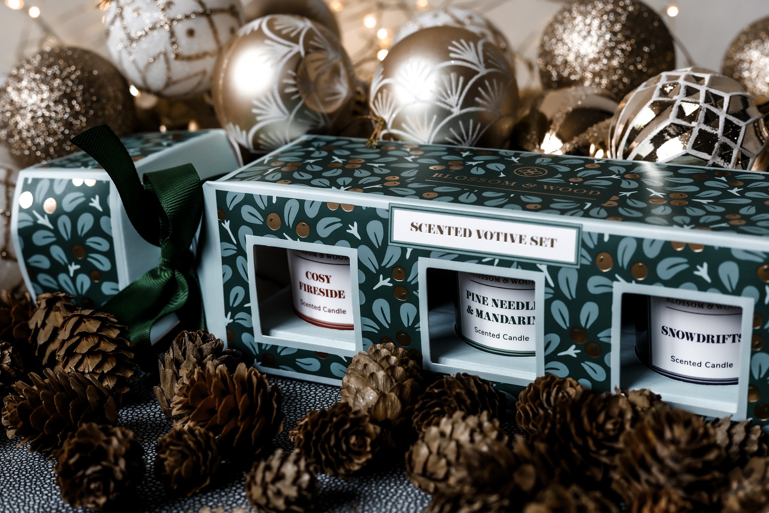 Festive scene with a scented votive candle set, surrounded by pinecones, ornaments, and twinkling lights.