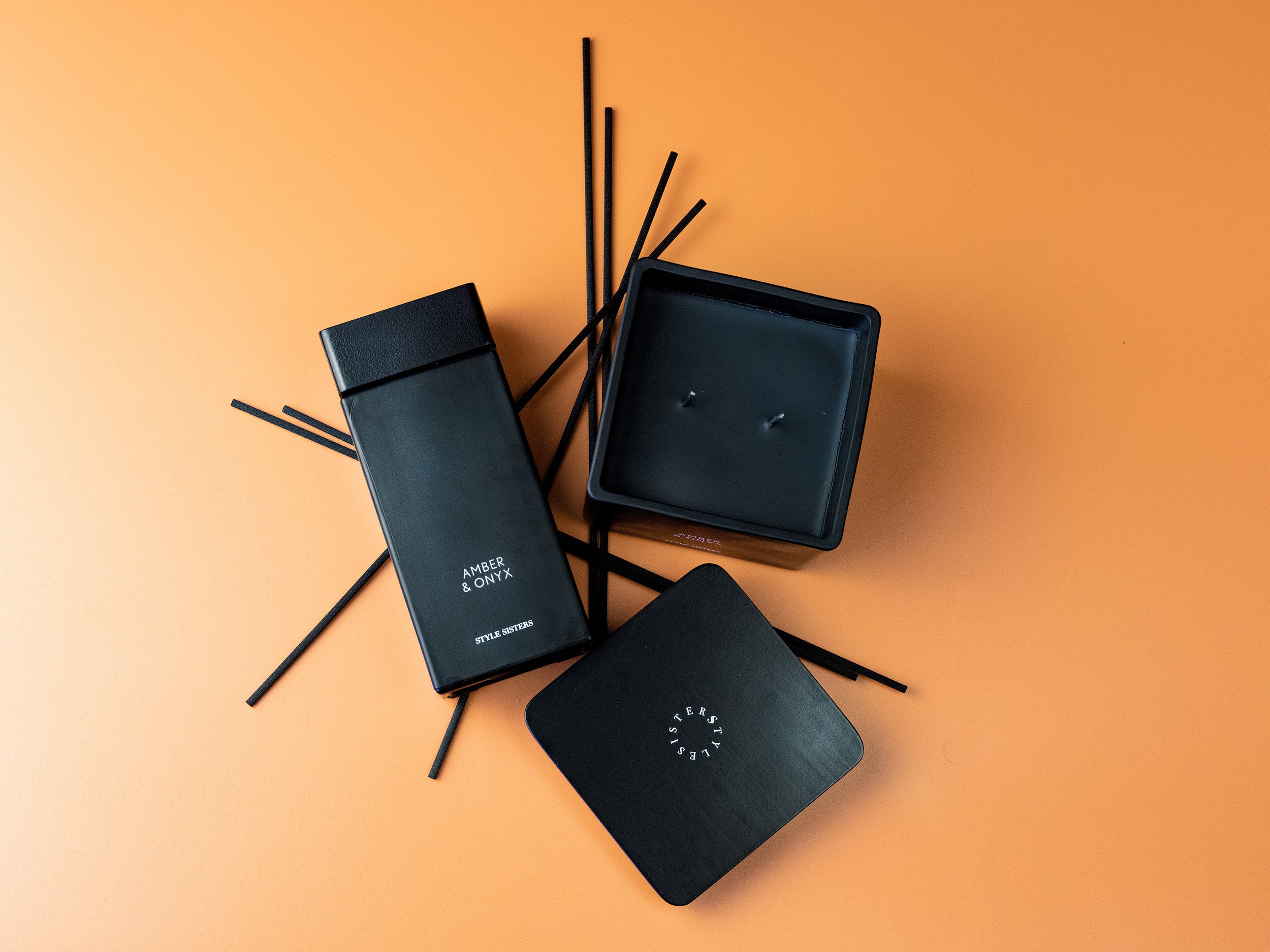 Black candle and diffuser set on orange background with black reeds