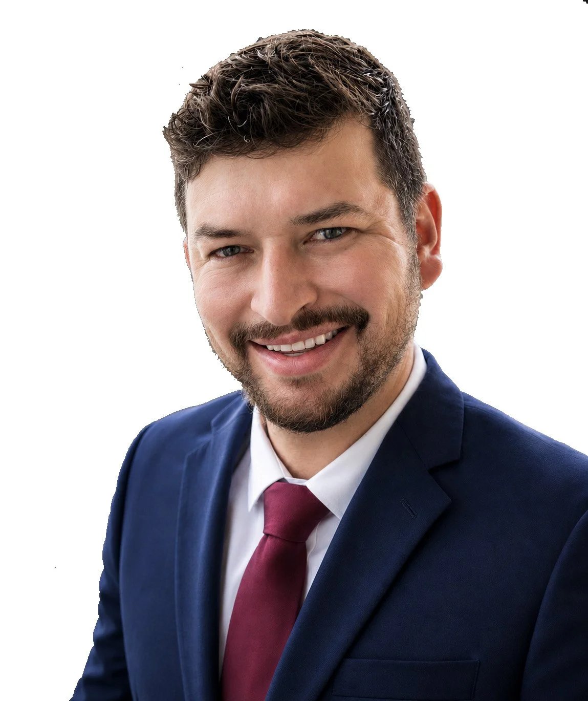 A young man with dark hair, blue eyes, and a friendly smile, wearing a dark patterned suit, light-colored shirt, and blue tie, against a plain light background.