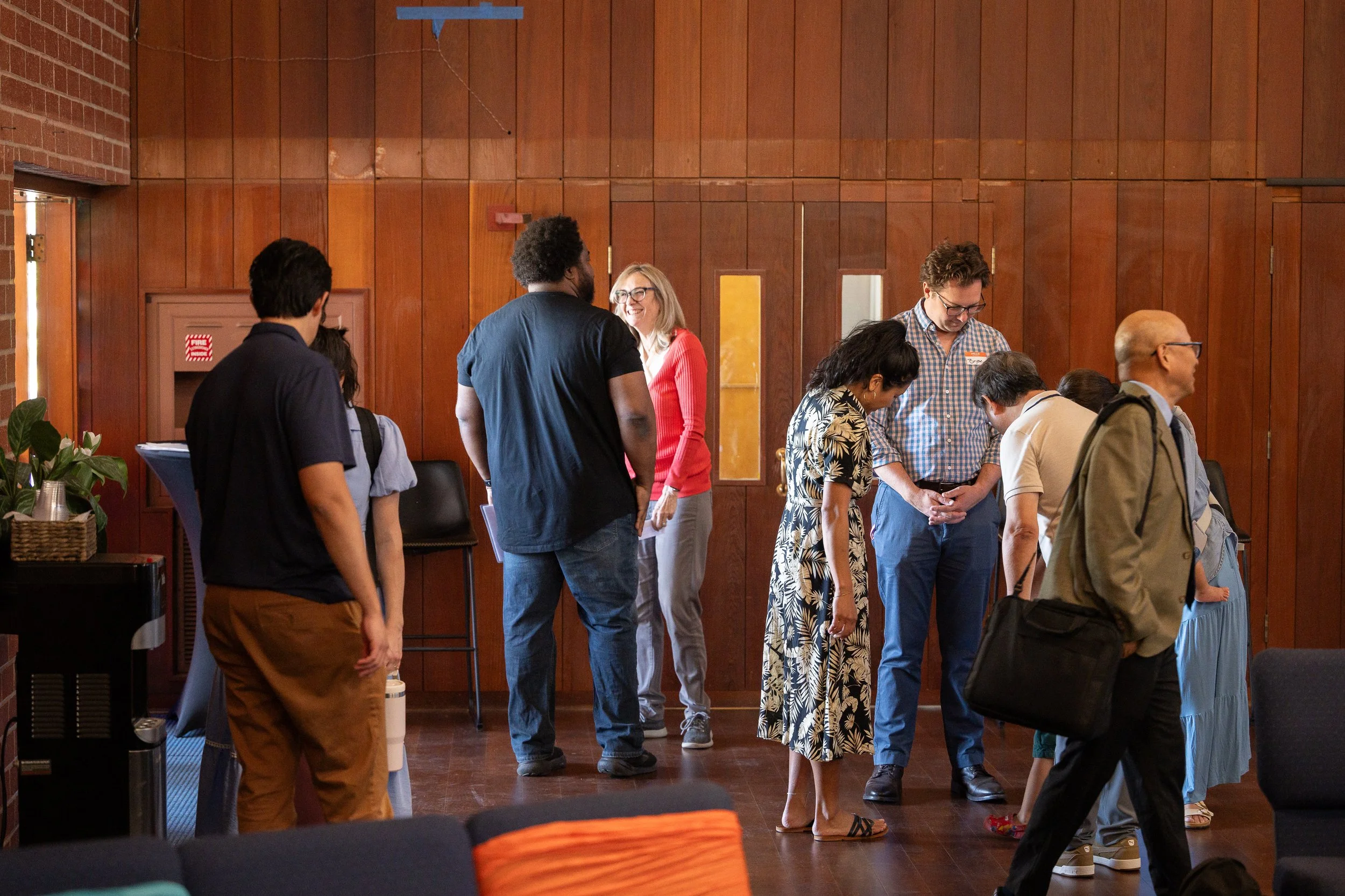 Group of people standing and bowing in a line, engaging in a prayer or moment of reflection in a room with wooden walls.