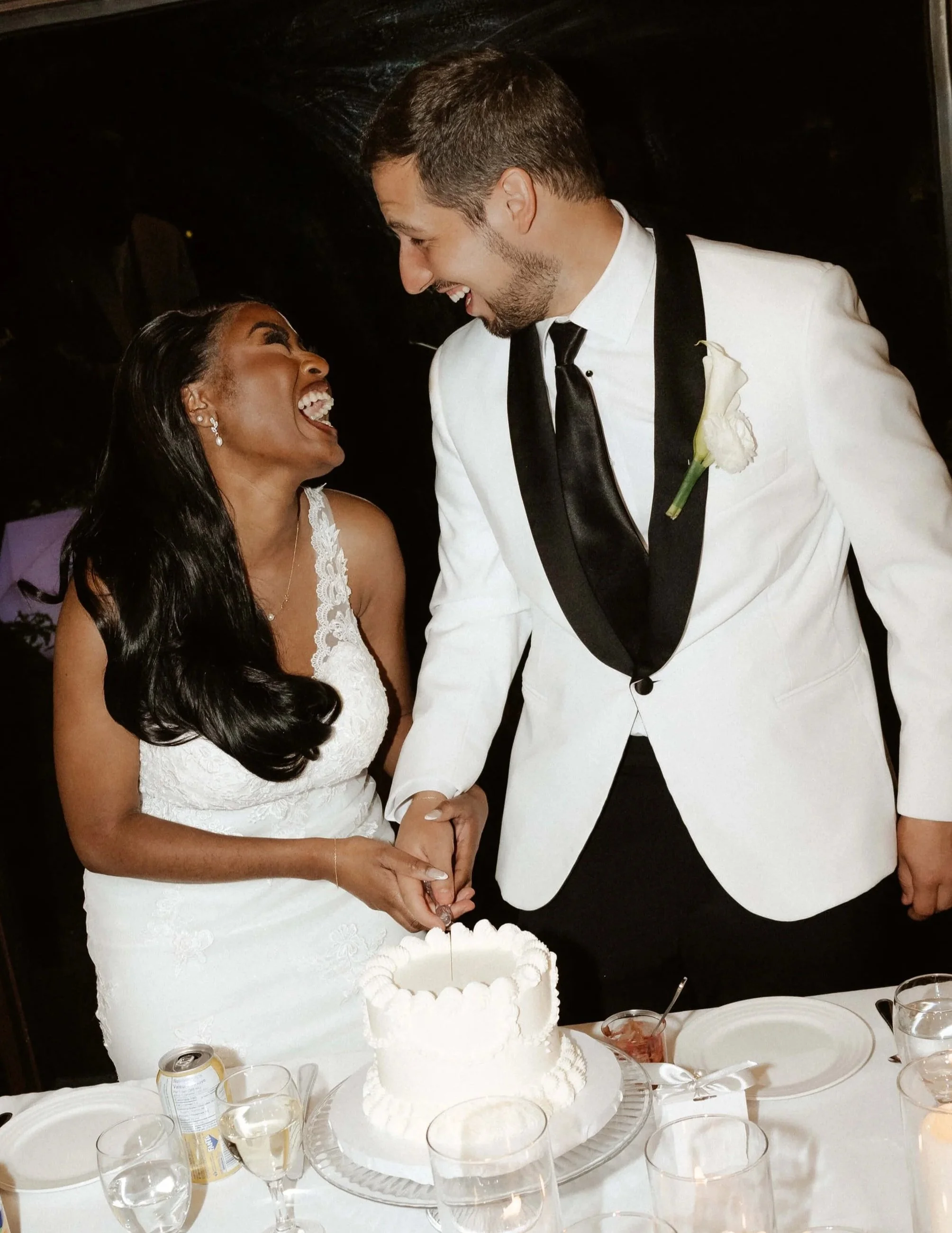 Une femme et un homme à leur réception de mariage coupent leur gâteau de mariage en partageant un fou rire ensemble